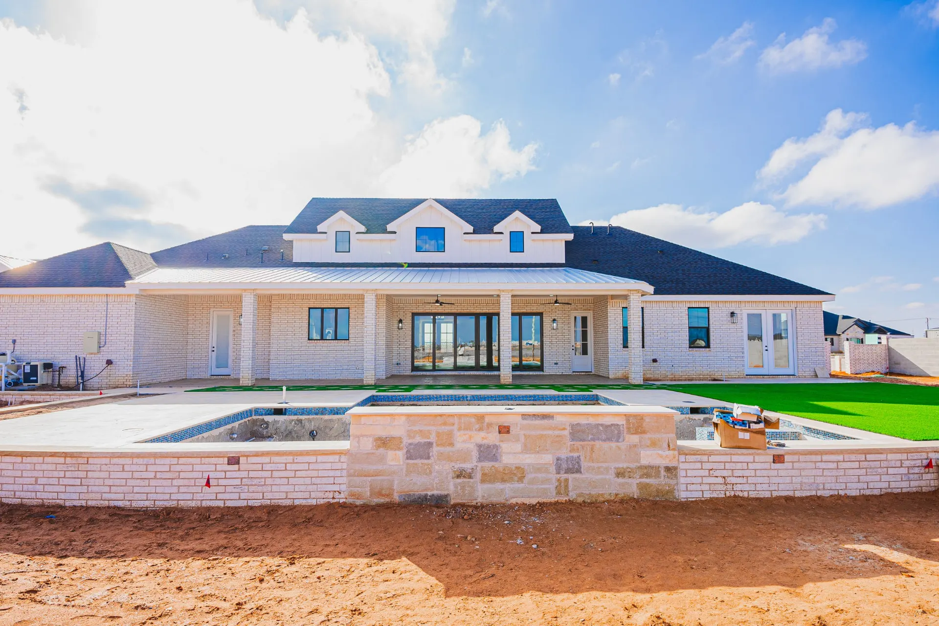 Rear elevation of 1602 NW 12th St with covered patio, stone seating wall and in-ground pool taking shape