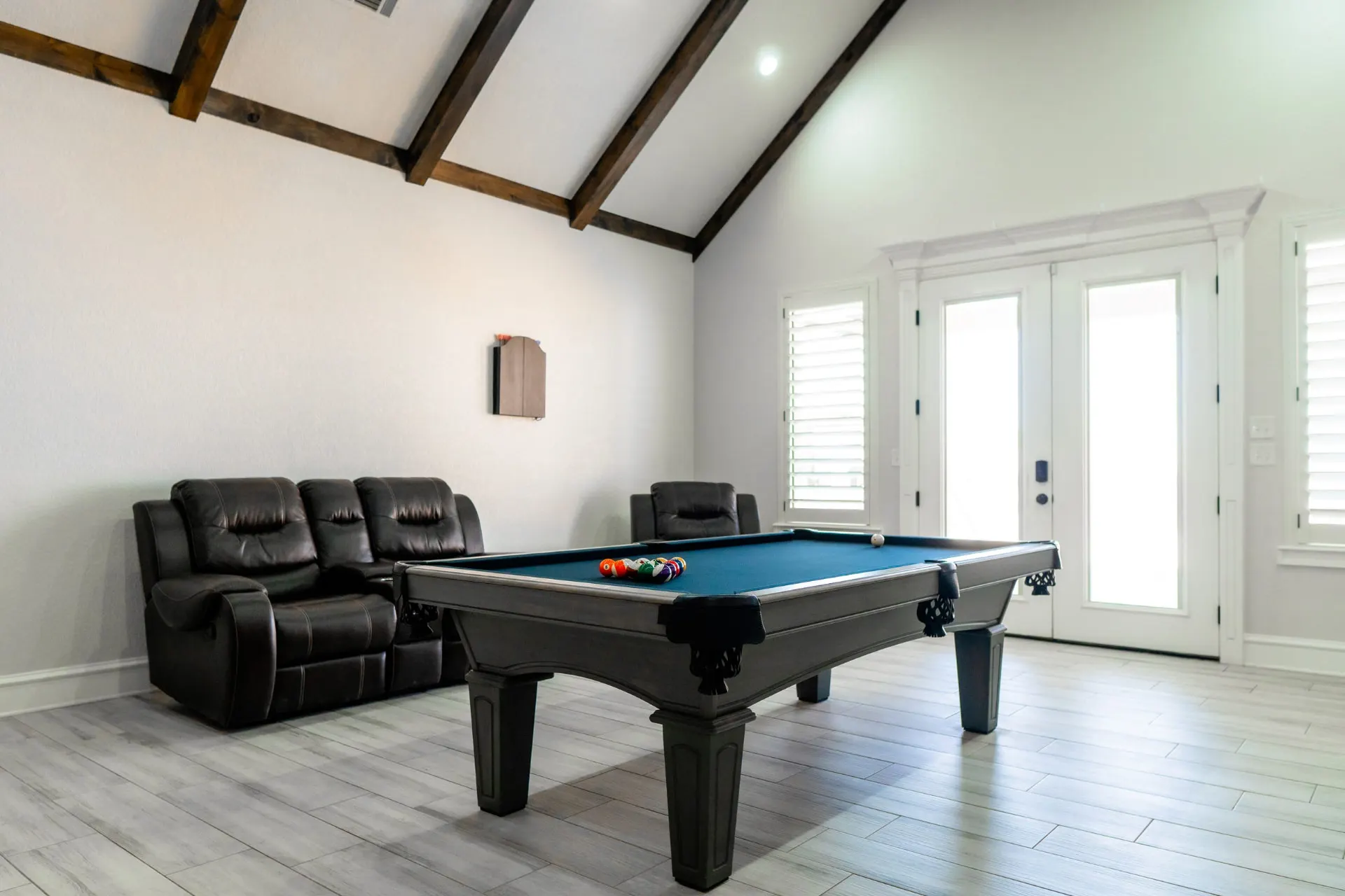 Game room at 1667 Eldenrod with a pool table under a vaulted beamed ceiling, leather recliners and shuttered French doors