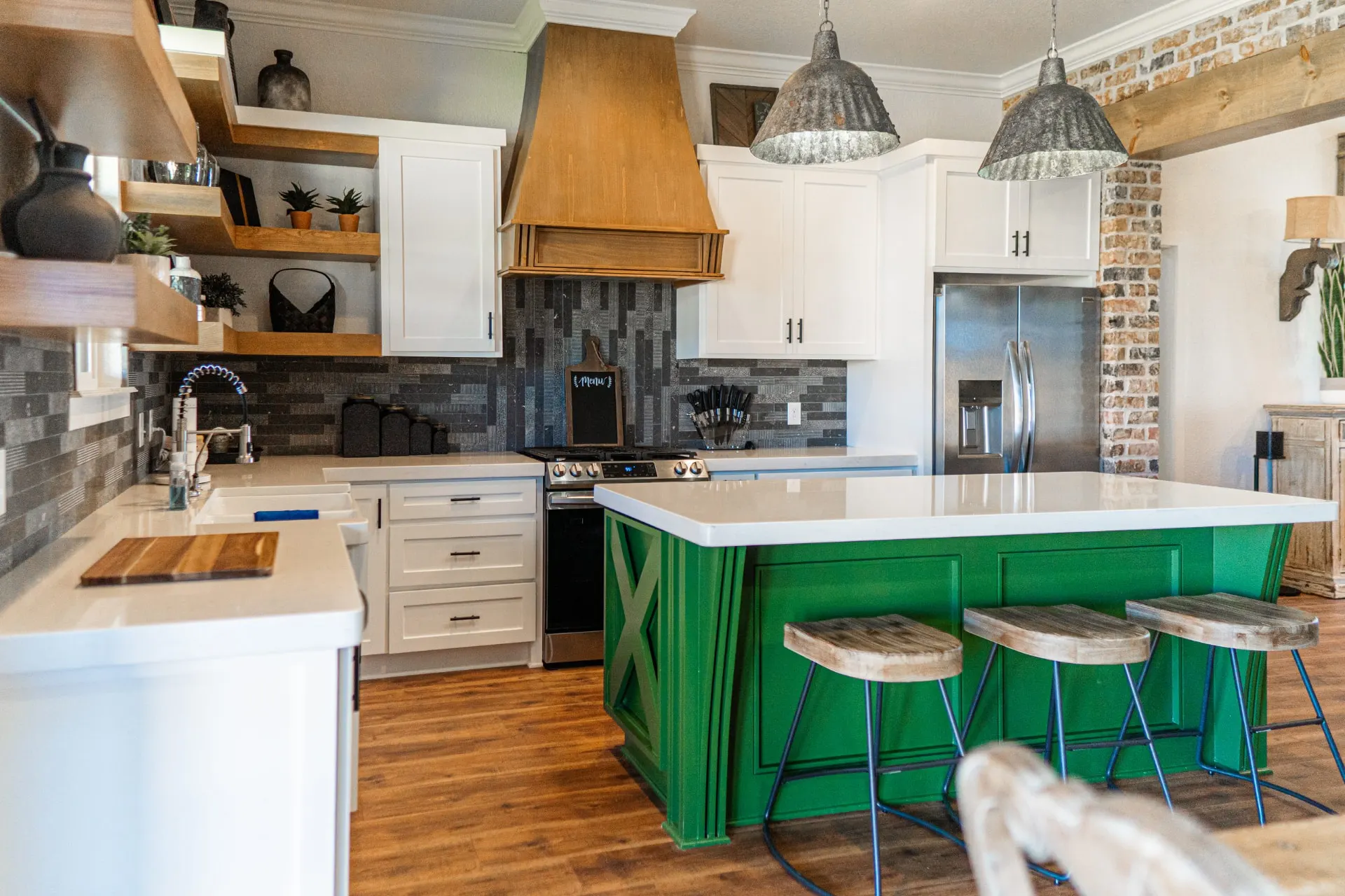 Kitchen at the K Ave Farmhouse with the green barn-door island, galvanized metal pendants, a copper-toned wood hood and a stainless side-by-side refrigerator