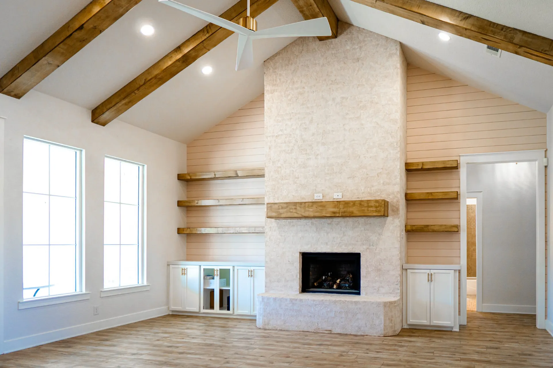 Alternate view of the vaulted great room at Sarai Home with the plastered fireplace, white shiplap shelving walls and recessed lighting