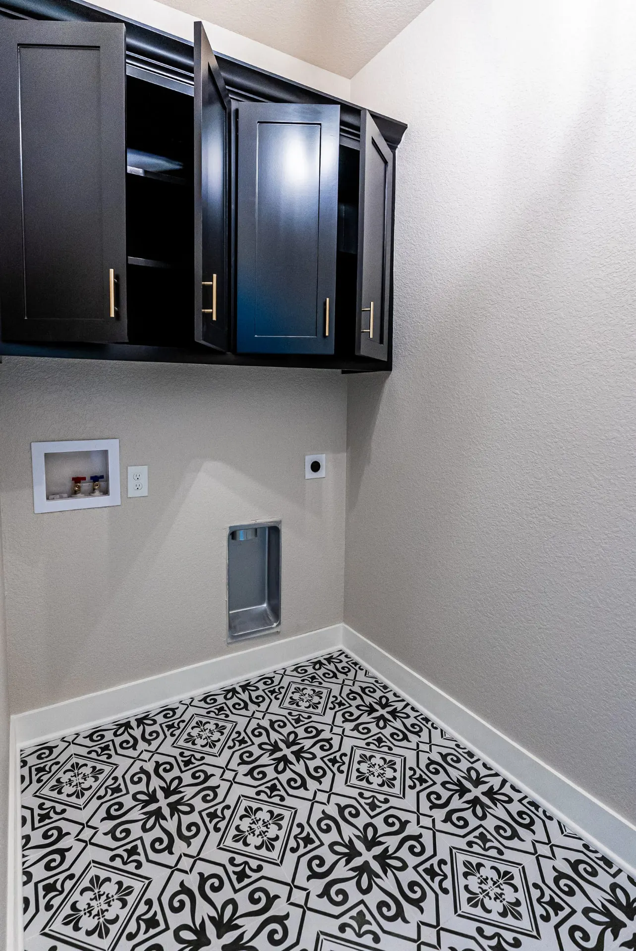 Laundry room at 708 K Ave with black upper cabinets, brass pulls, a washer drip pan and dramatic black-and-white patterned floor tile