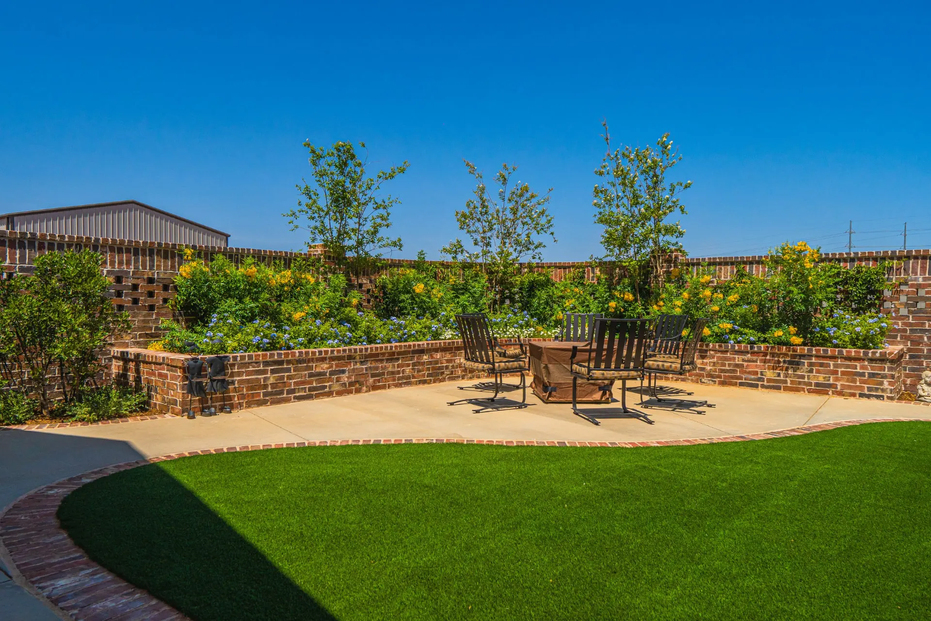 Wide backyard view at the Wraparound Porch Home with green turf edged in brick, a fire-pit seating area and a brick privacy wall