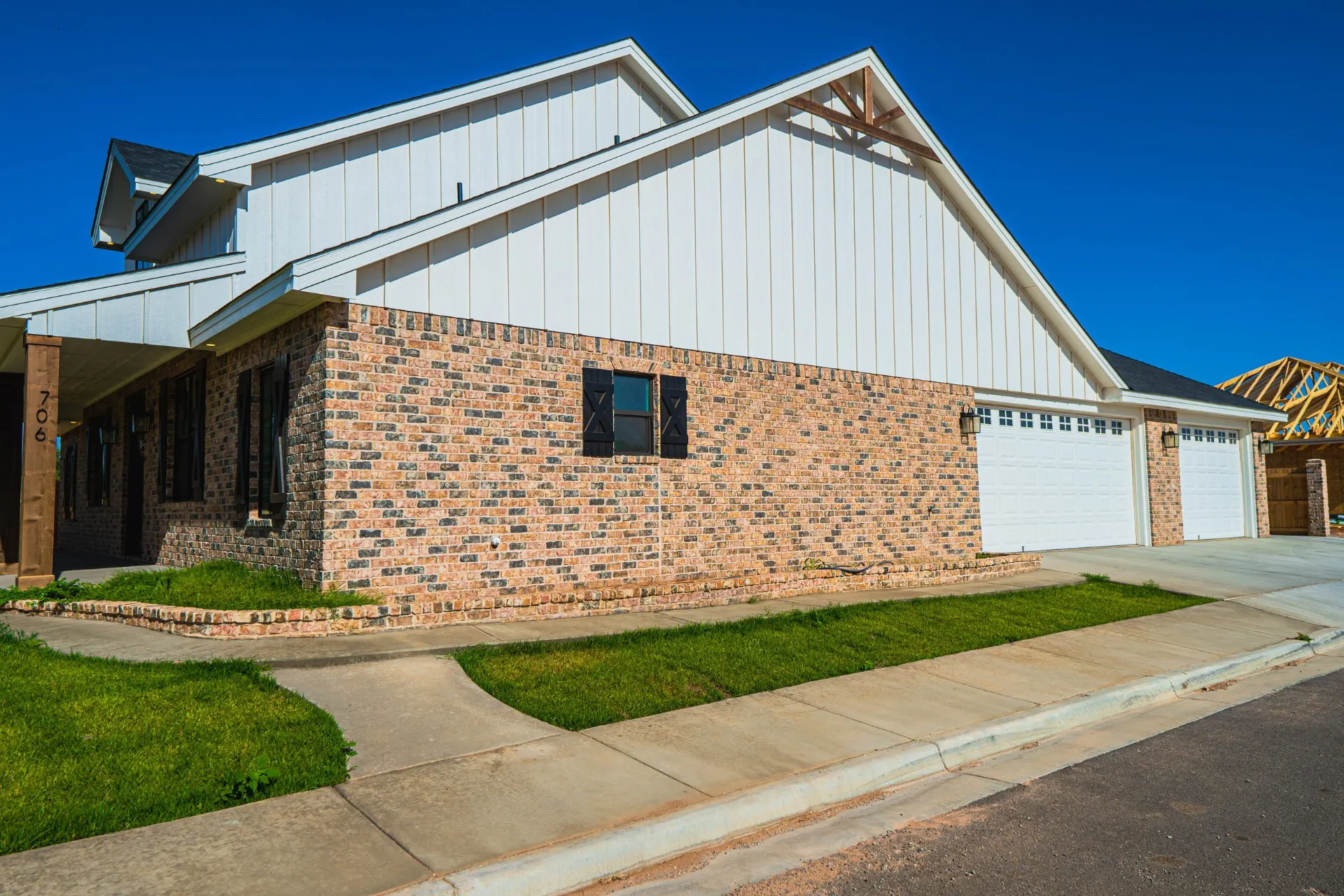 Side elevation of the K Ave Farmhouse with twin white garage doors, a brick lower level and white board-and-batten gables