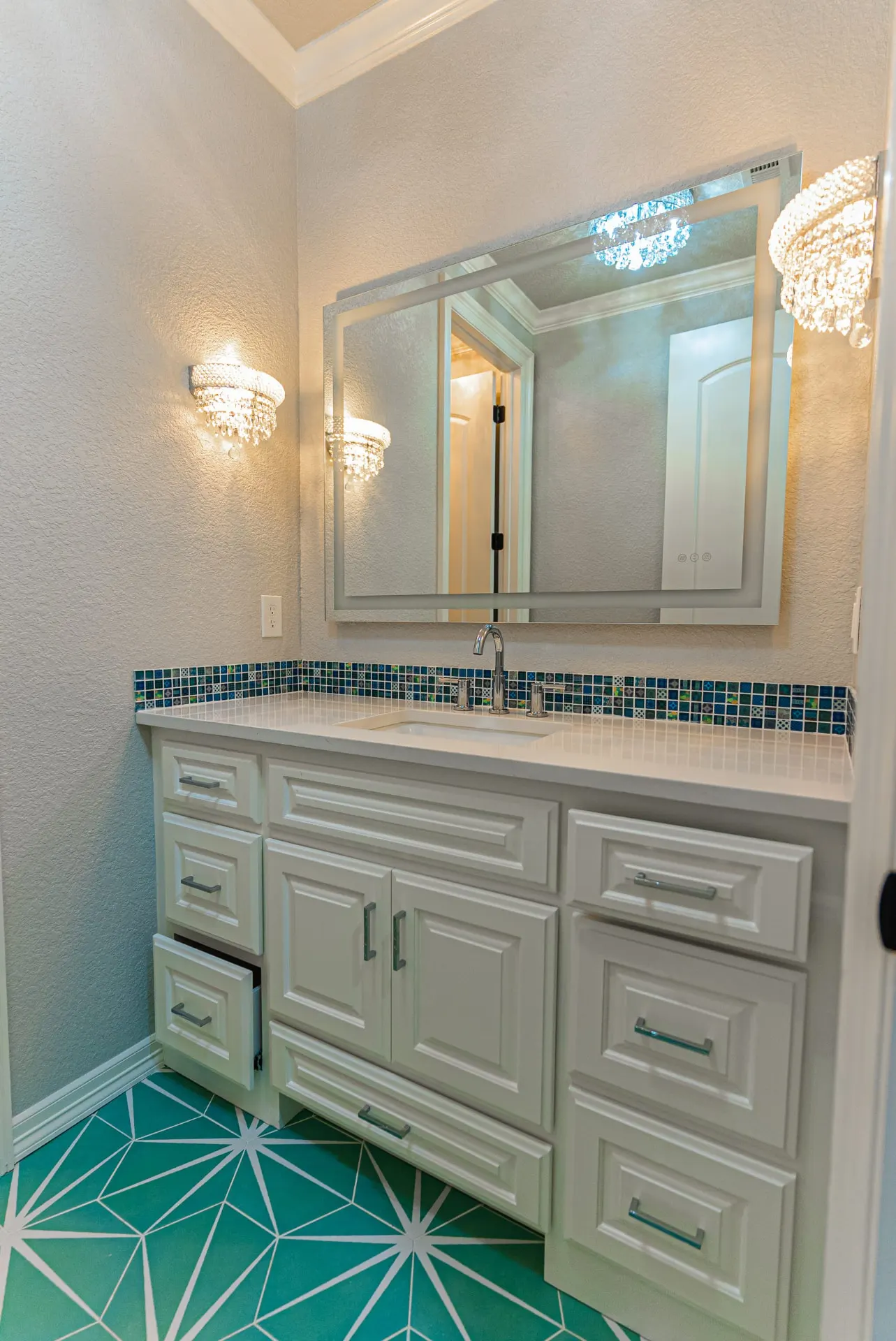 Bathroom vanity at 1511 NW 12th St with white cabinetry, crystal sconces, blue mosaic accent and teal geometric floor tile