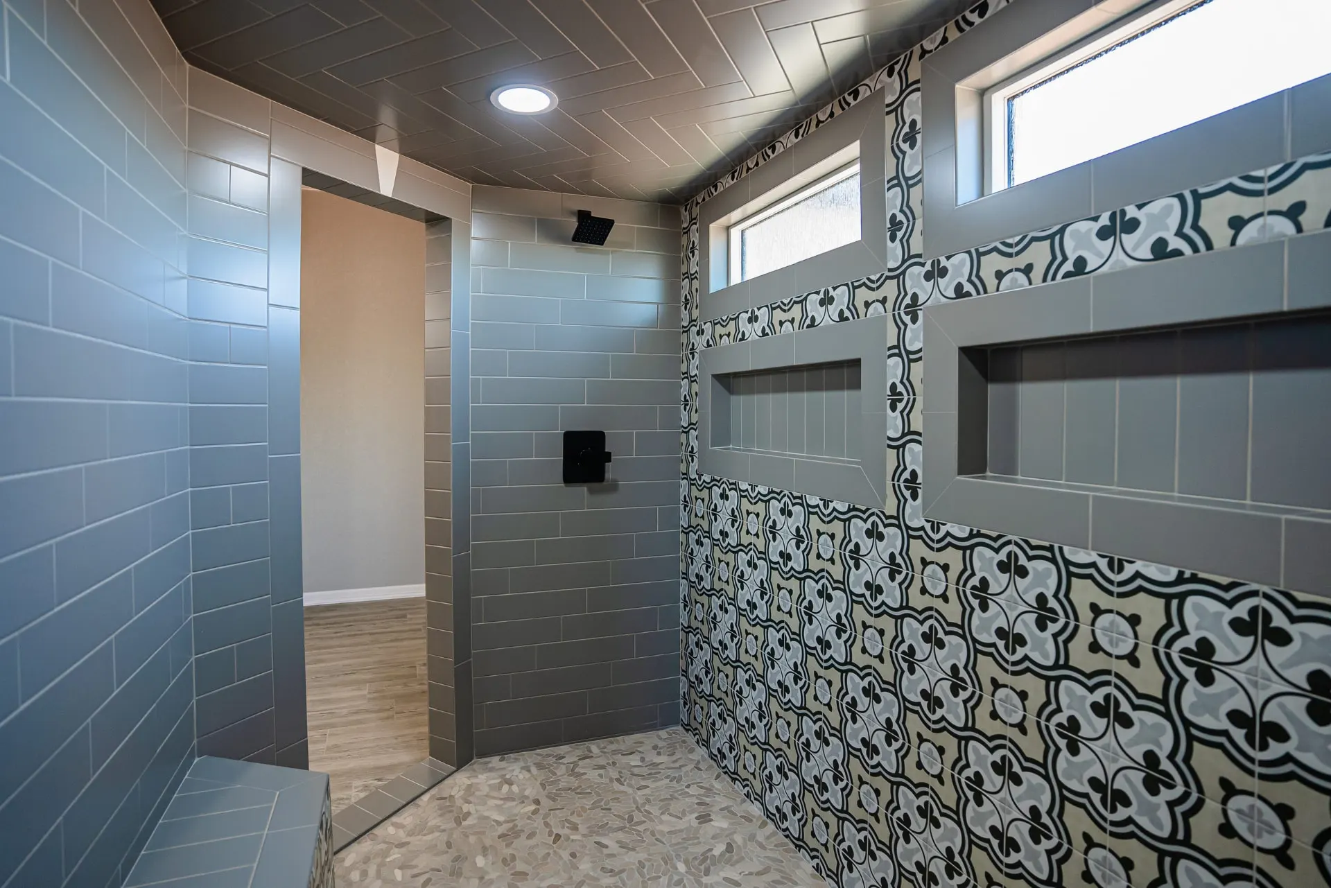 Walk-in shower at the Eliam St Home with blue-grey subway tile, black fixtures, quatrefoil patterned tile niches and a pebble floor