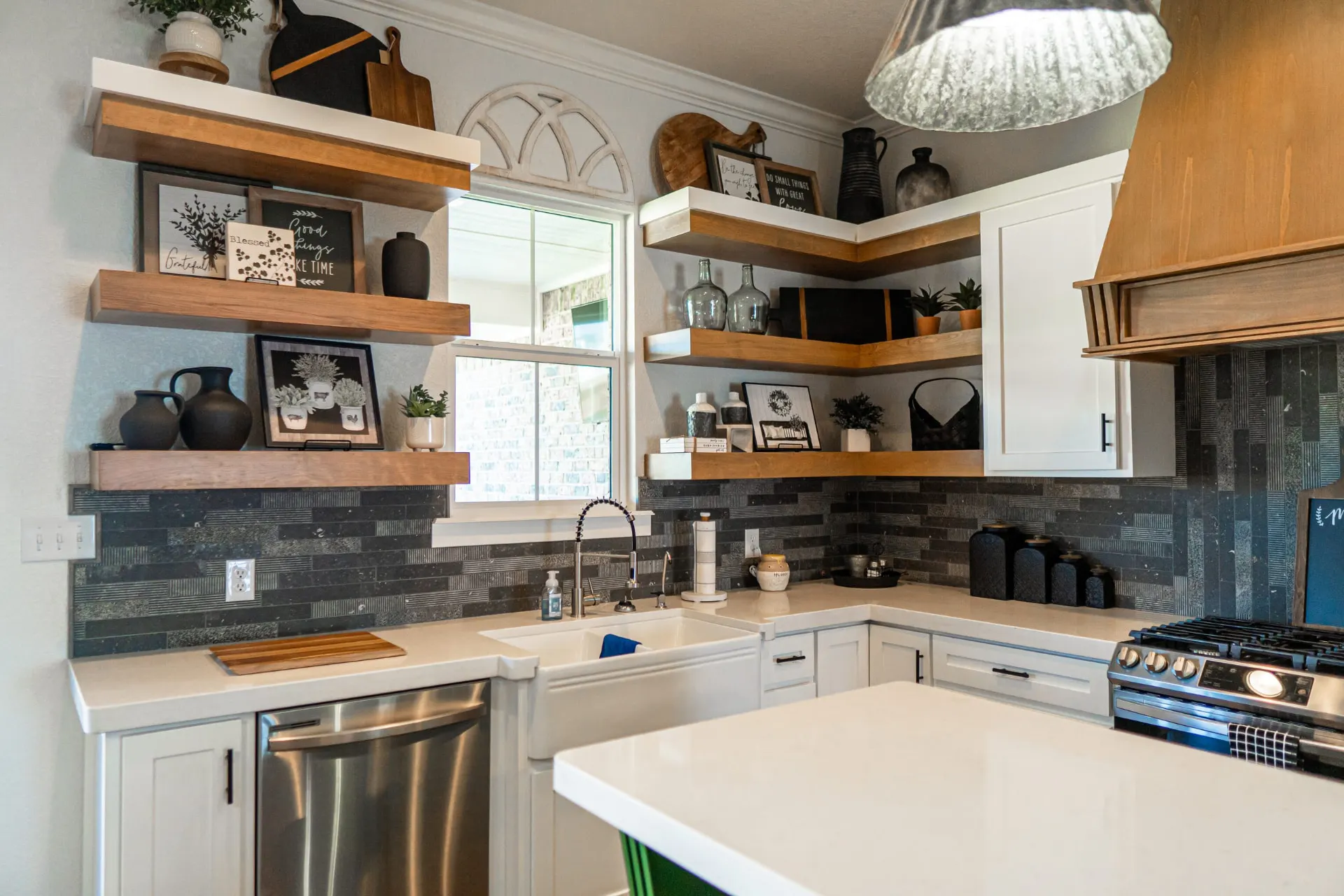 Kitchen corner at the K Ave Farmhouse with a white farmhouse sink, white cabinetry, floating wood shelves and a charcoal stacked-tile backsplash