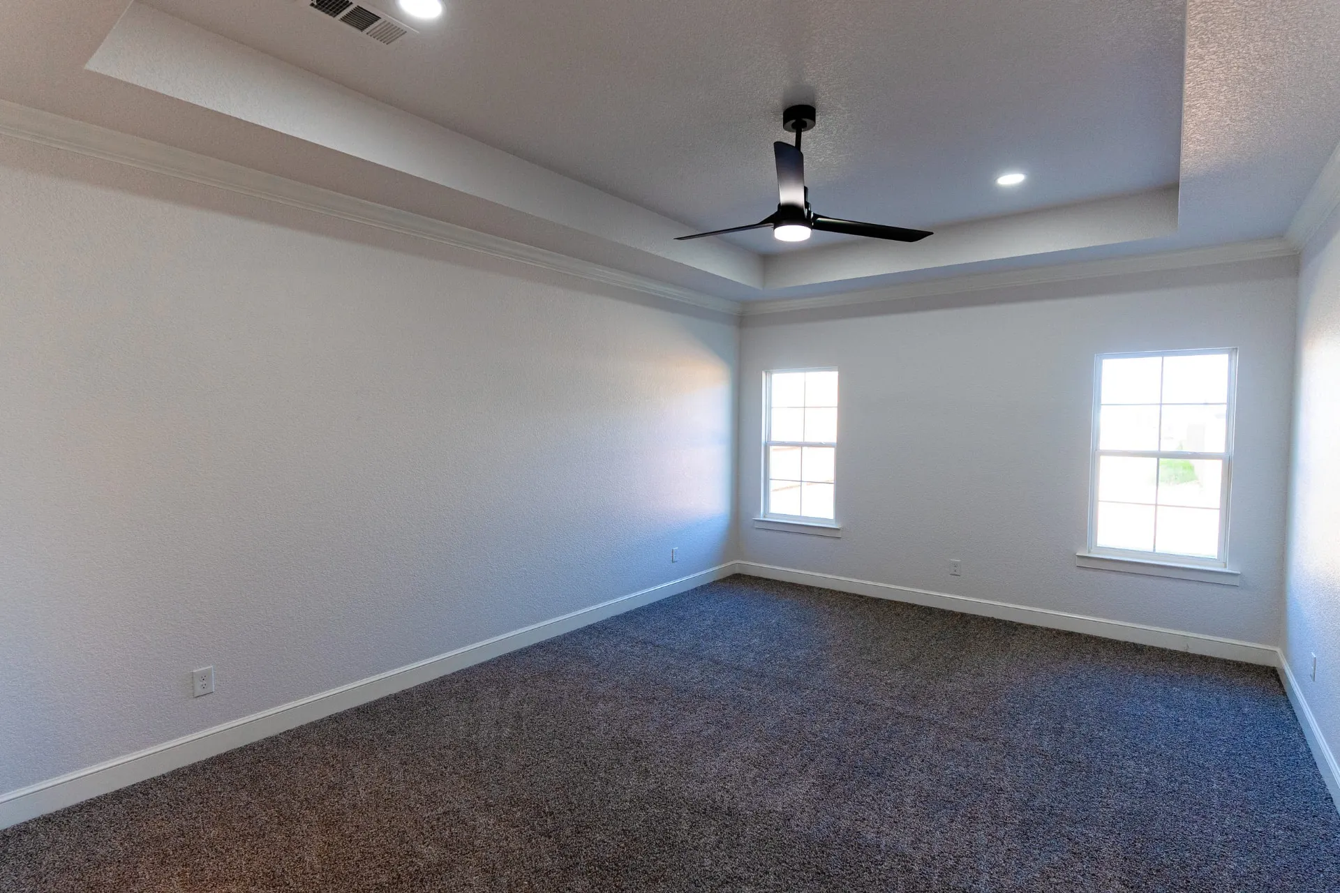 Bedroom at 718 K Ave with a tray ceiling, modern ceiling fan, gray carpet and two multi-pane windows