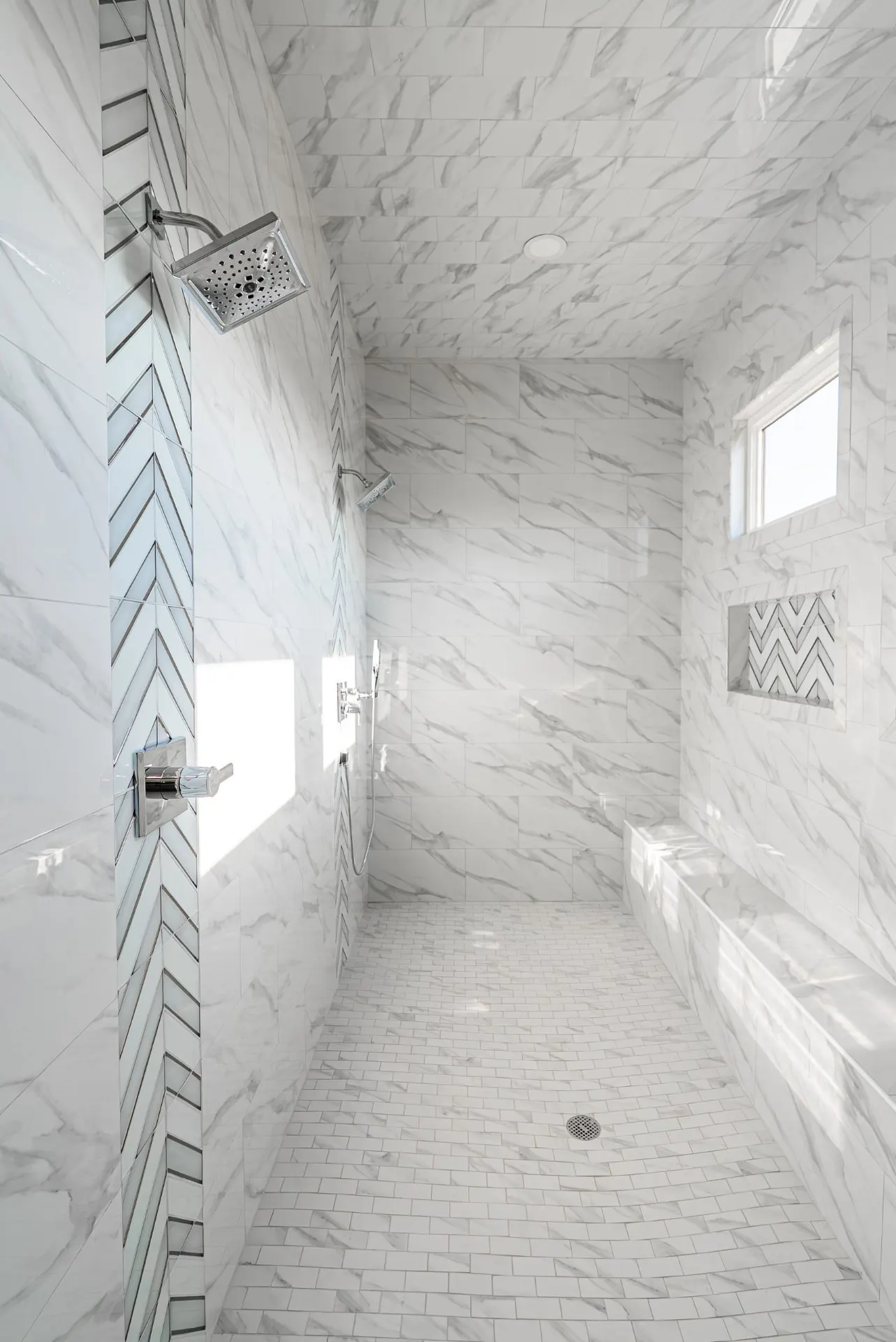 Walk-in shower with marble-look tile, chevron accent strip, bench and twin showerheads at 27 Santiago Mission Dr
