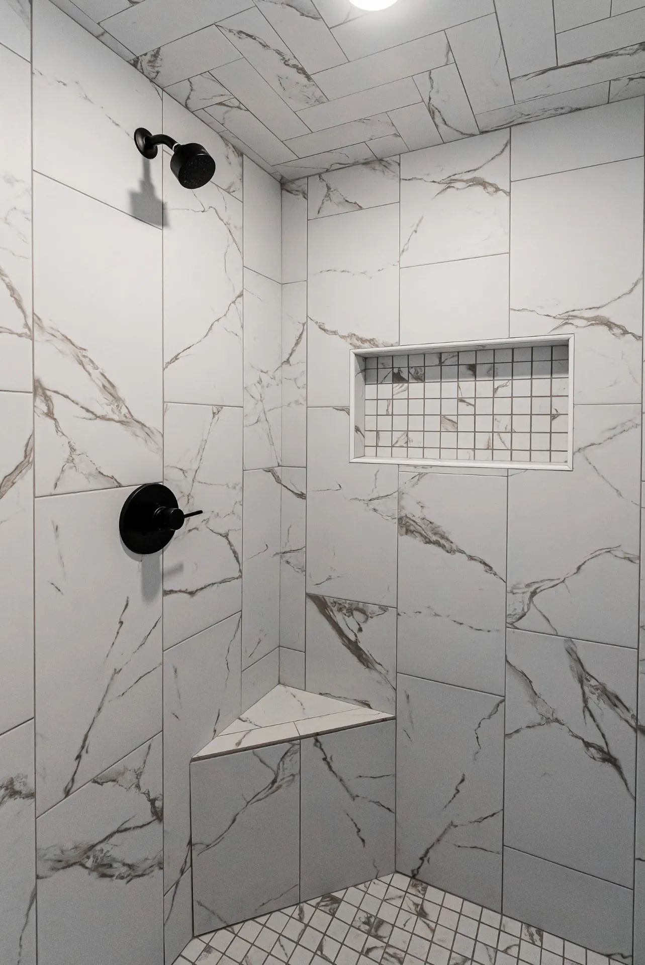 Walk-in shower at 708 K Ave with marble-look tile, a herringbone ceiling, mosaic niche and corner bench over pebble-style floor tile