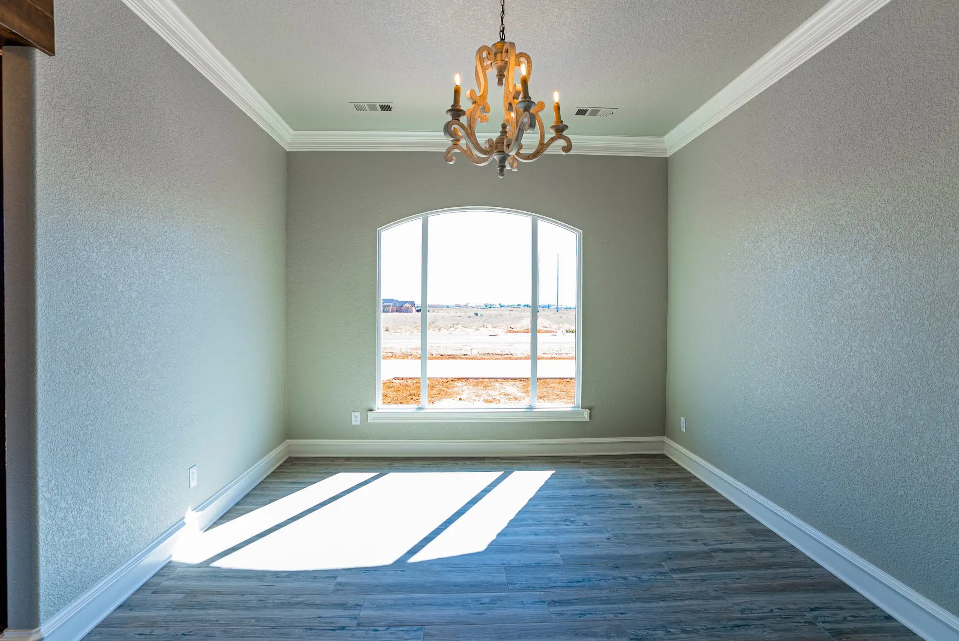 Formal dining room at the Eliam St Home with a wood chandelier and an arched window looking out to the open field