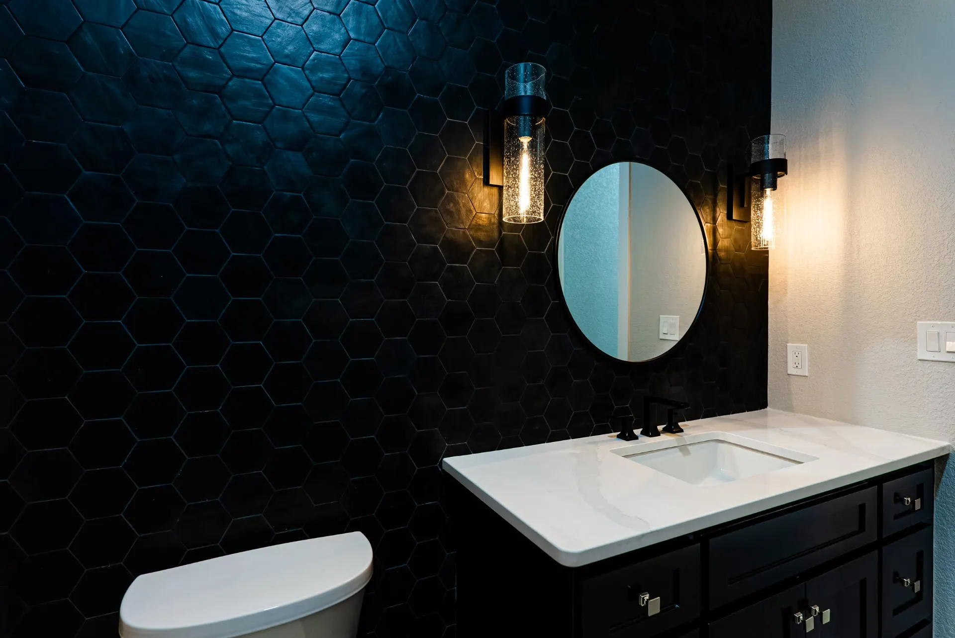Powder room with a black hexagon tile wall, round mirror and seeded-glass sconces at 27 Santiago Mission Dr