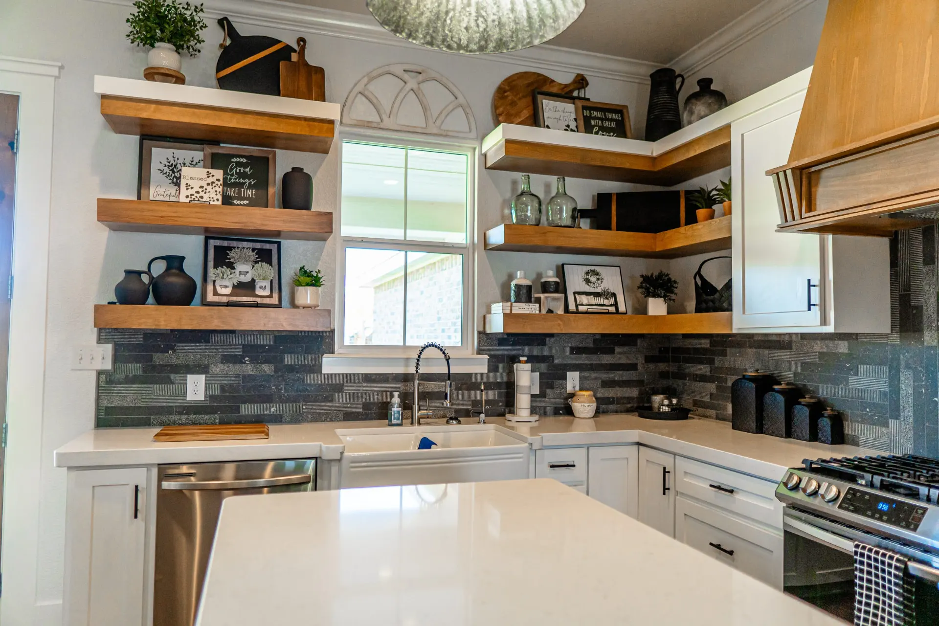 Kitchen corner at the K Ave Farmhouse from the island, with the farmhouse sink, floating wood shelves, a chalkboard menu board and a seeded glass pendant