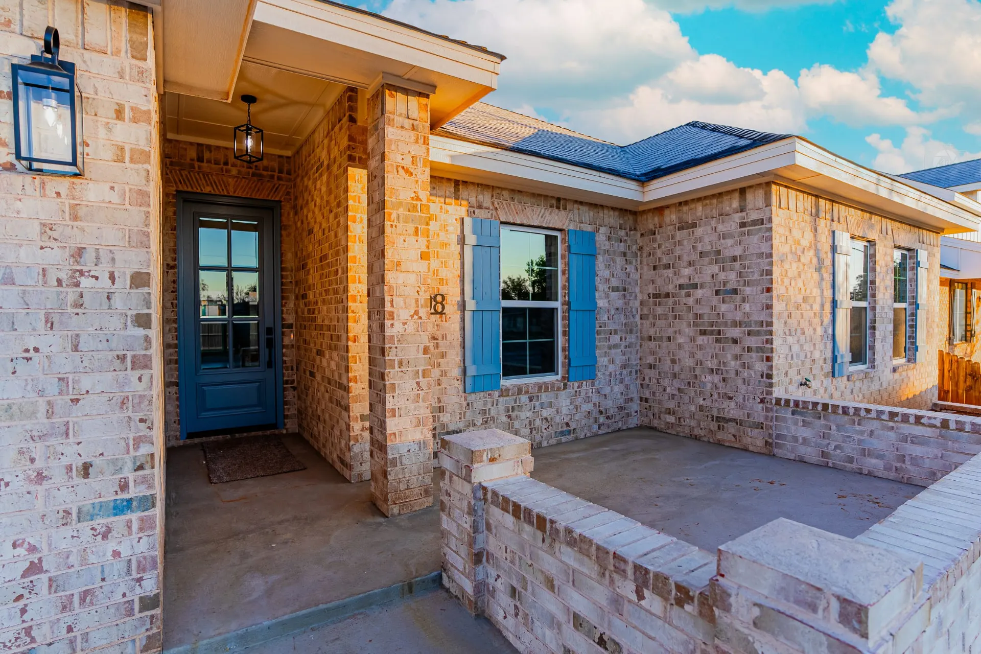 Covered front porch at 708 K Ave with black lantern sconces, blue glass-paneled front door and brick columns