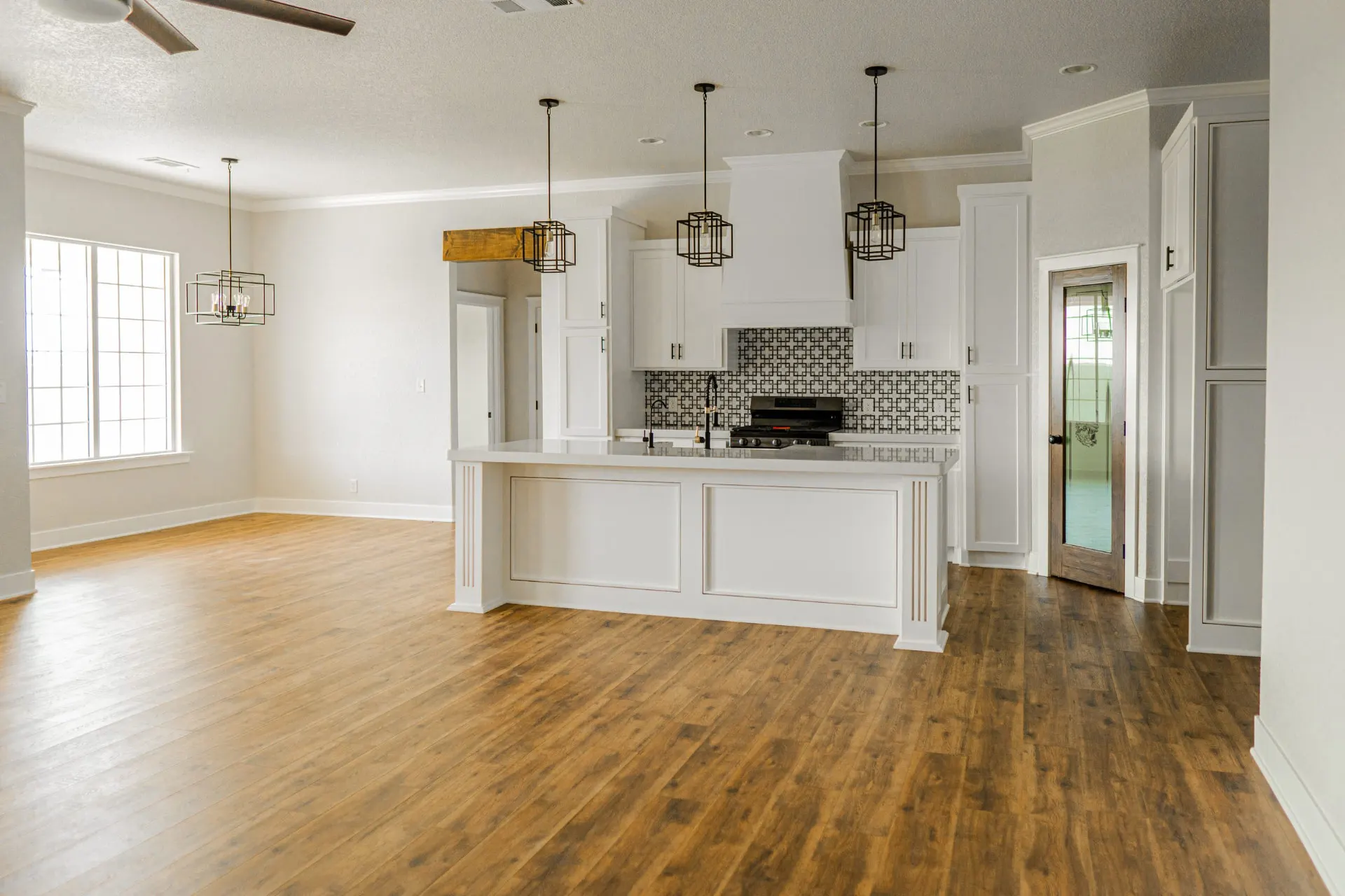 Kitchen at 1615 NW 12th St with white cabinetry, large island, black geometric backsplash and cage pendants over the range