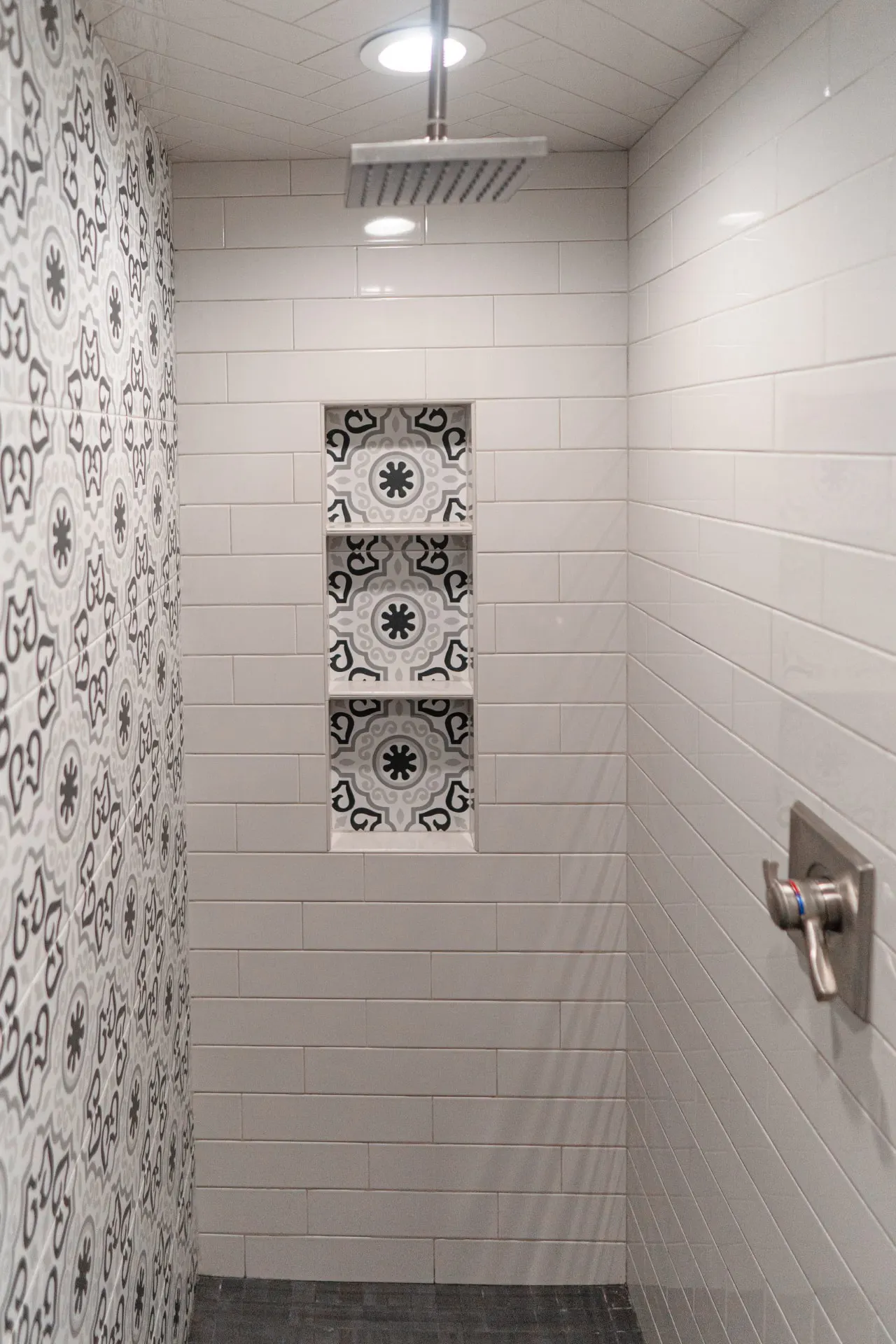 Walk-in shower at the K Ave Farmhouse with white subway walls, a black-and-white patterned mosaic niche and a rain head