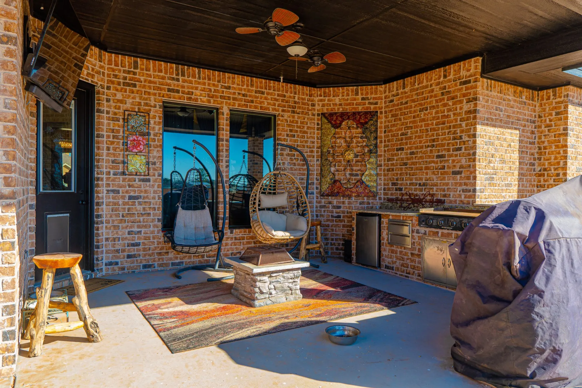 Covered patio and outdoor kitchen with a stone fire pit, hanging egg chairs, griddle and fridge under a dark-stained ceiling at 8821 Shawn Dr
