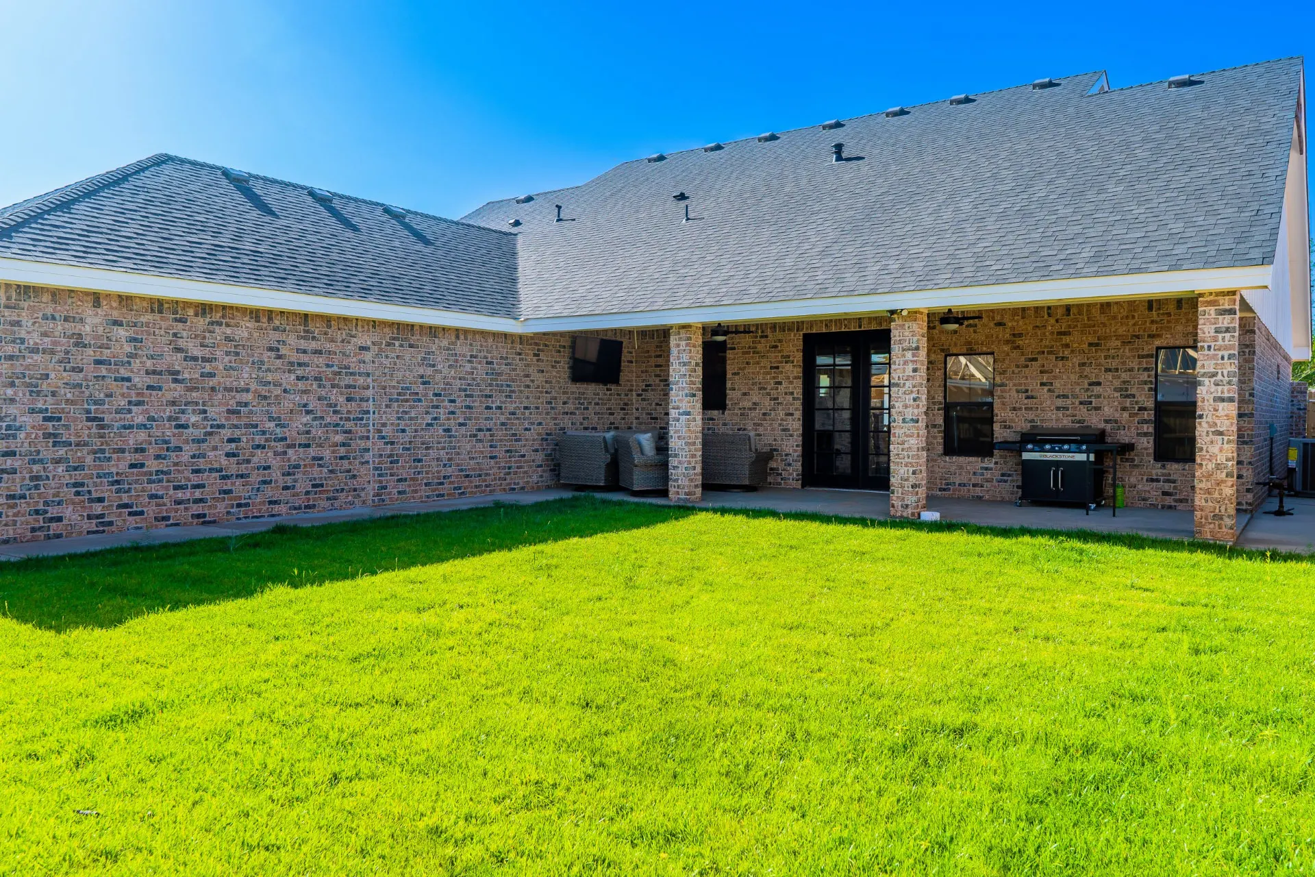 Covered rear patio at the K Ave Farmhouse with turf, wicker seating, a mounted TV and a Blackstone-style grill