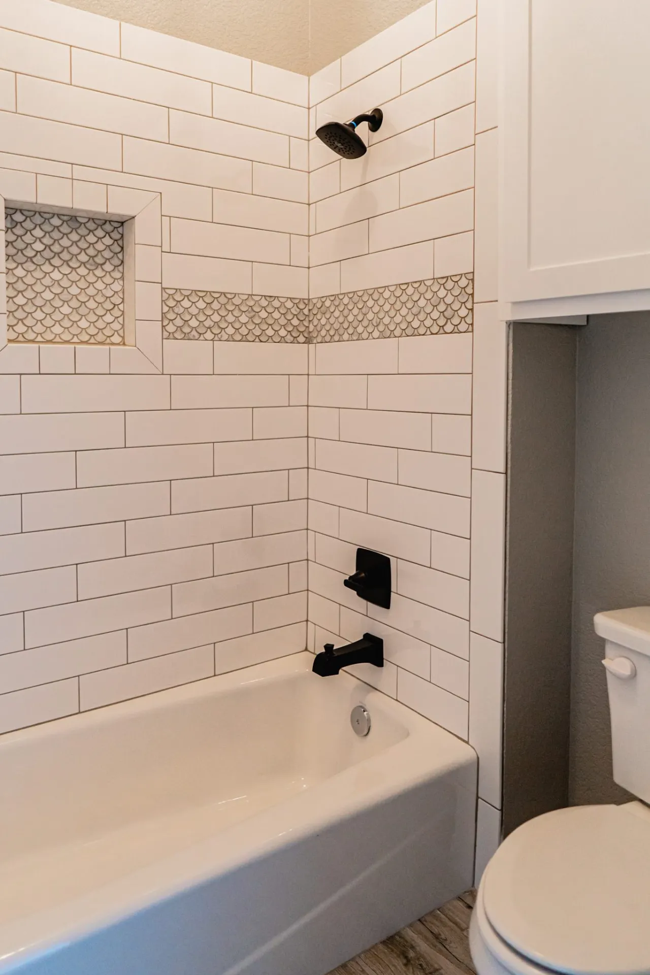 Tub and shower at the 12th St Home in white subway tile with a marble fish-scale mosaic band and matching recessed niche