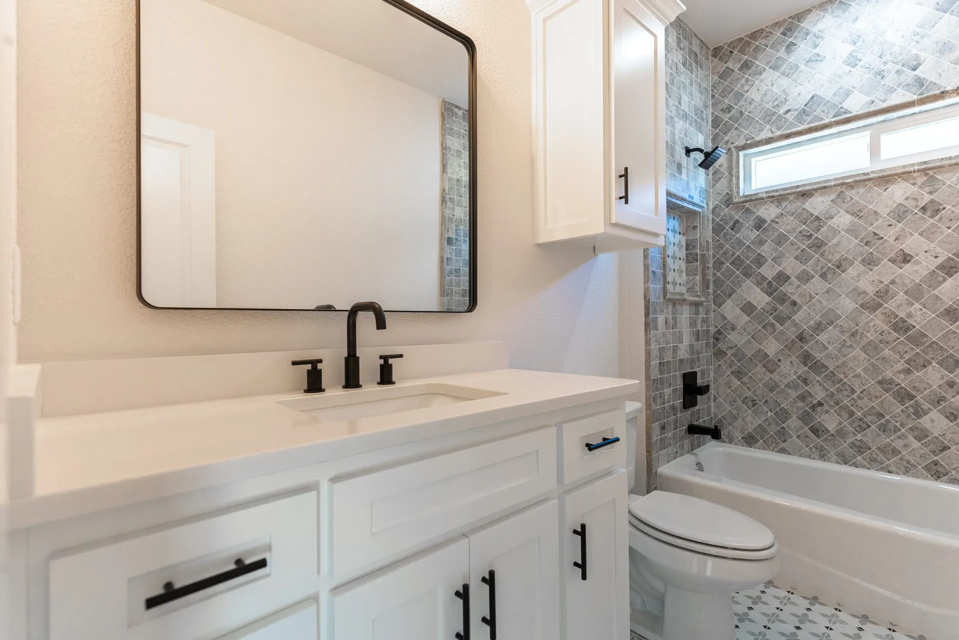 Guest bath at 718 K Ave with a white vanity, matte black fixtures and a diamond-set stone tile tub surround