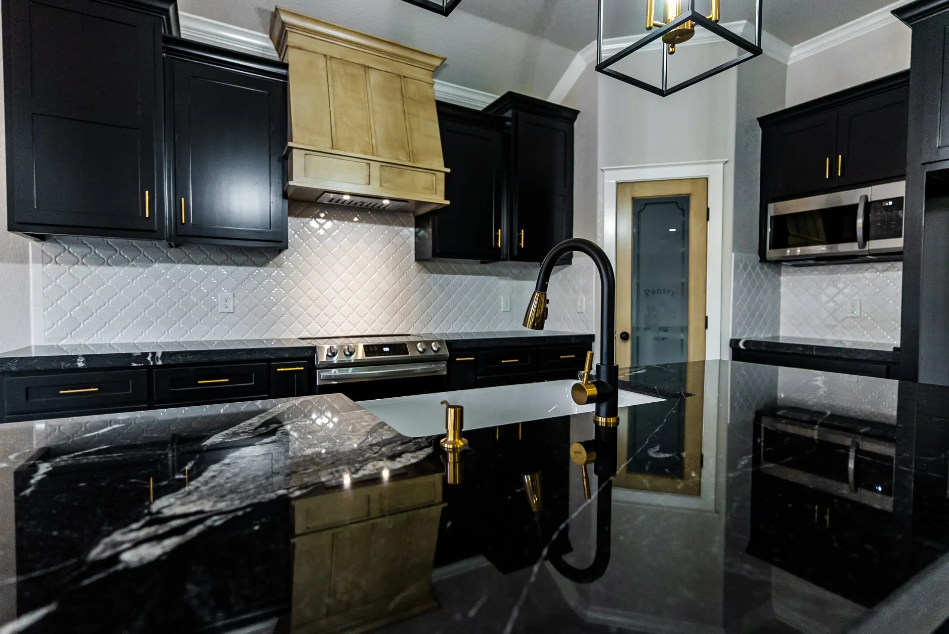 Black marble island at 708 K Ave with a farmhouse sink, black gooseneck faucet and a stained wood range hood beyond