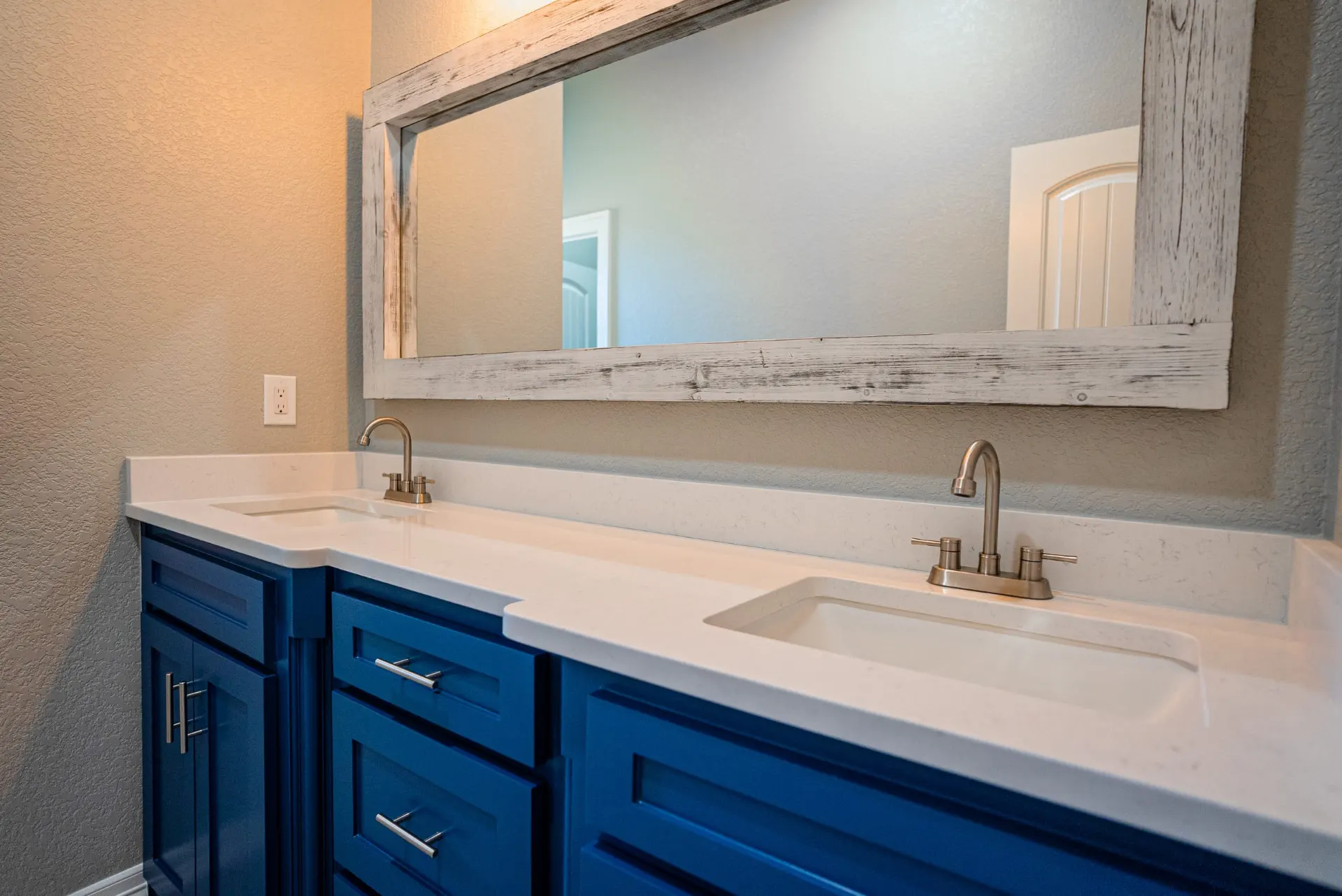 Close-up of the Eliam St Home bath vanity with cobalt blue cabinetry, brushed-nickel faucets, white quartz top and a whitewashed wood-frame mirror