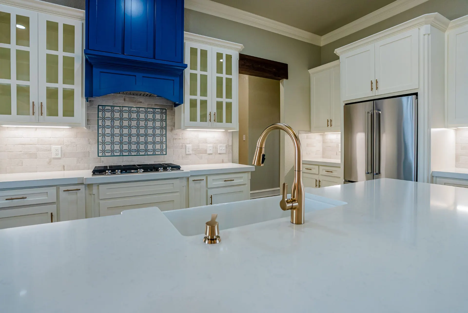 Close-up at the Eliam St Home of the farmhouse sink and brass bridge faucet under the cobalt hood and patterned tile backsplash