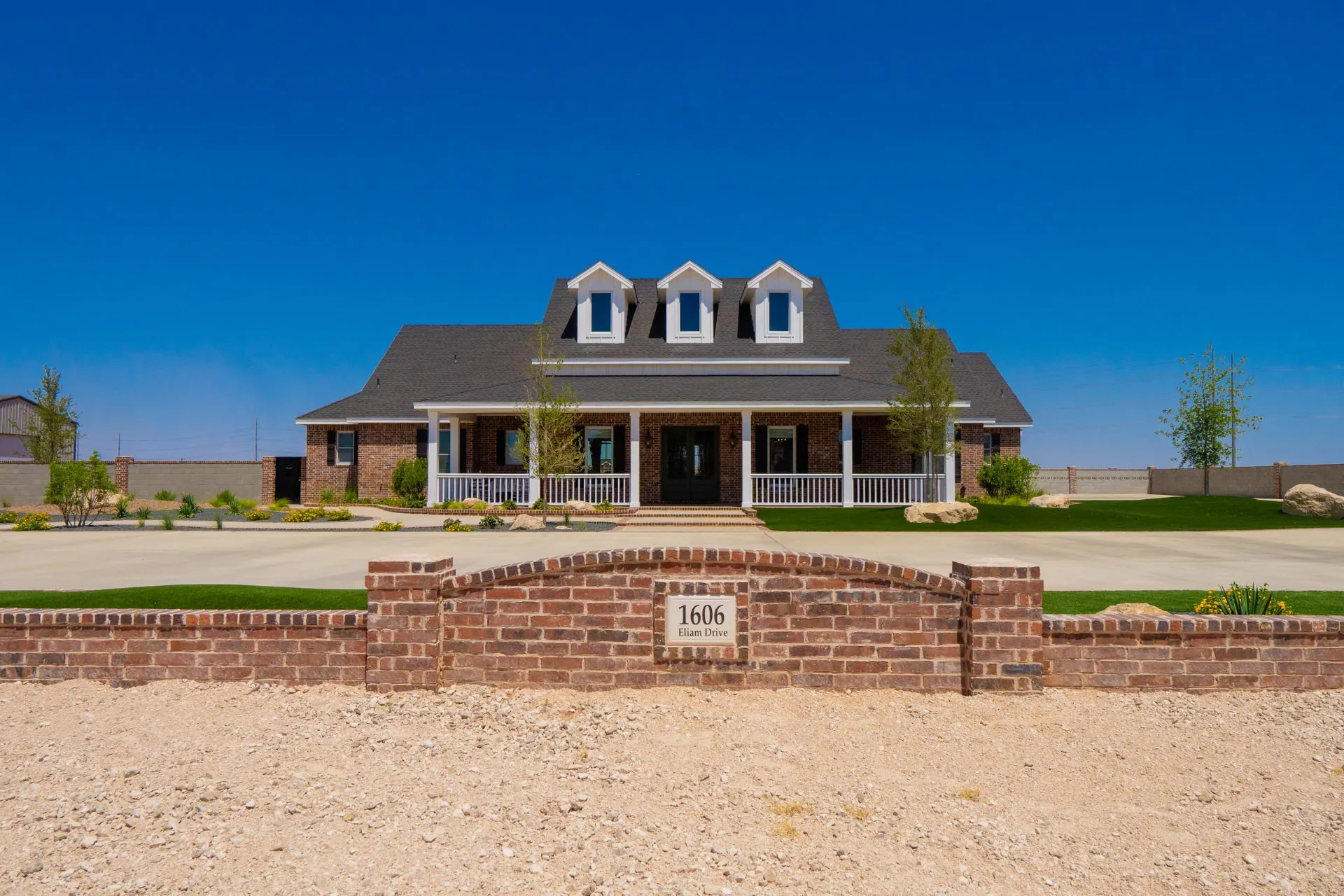 Front entrance of the Wraparound Porch Home behind the brick street marker at 1606 Eliam Drive, with a symmetrical porch and manicured yard