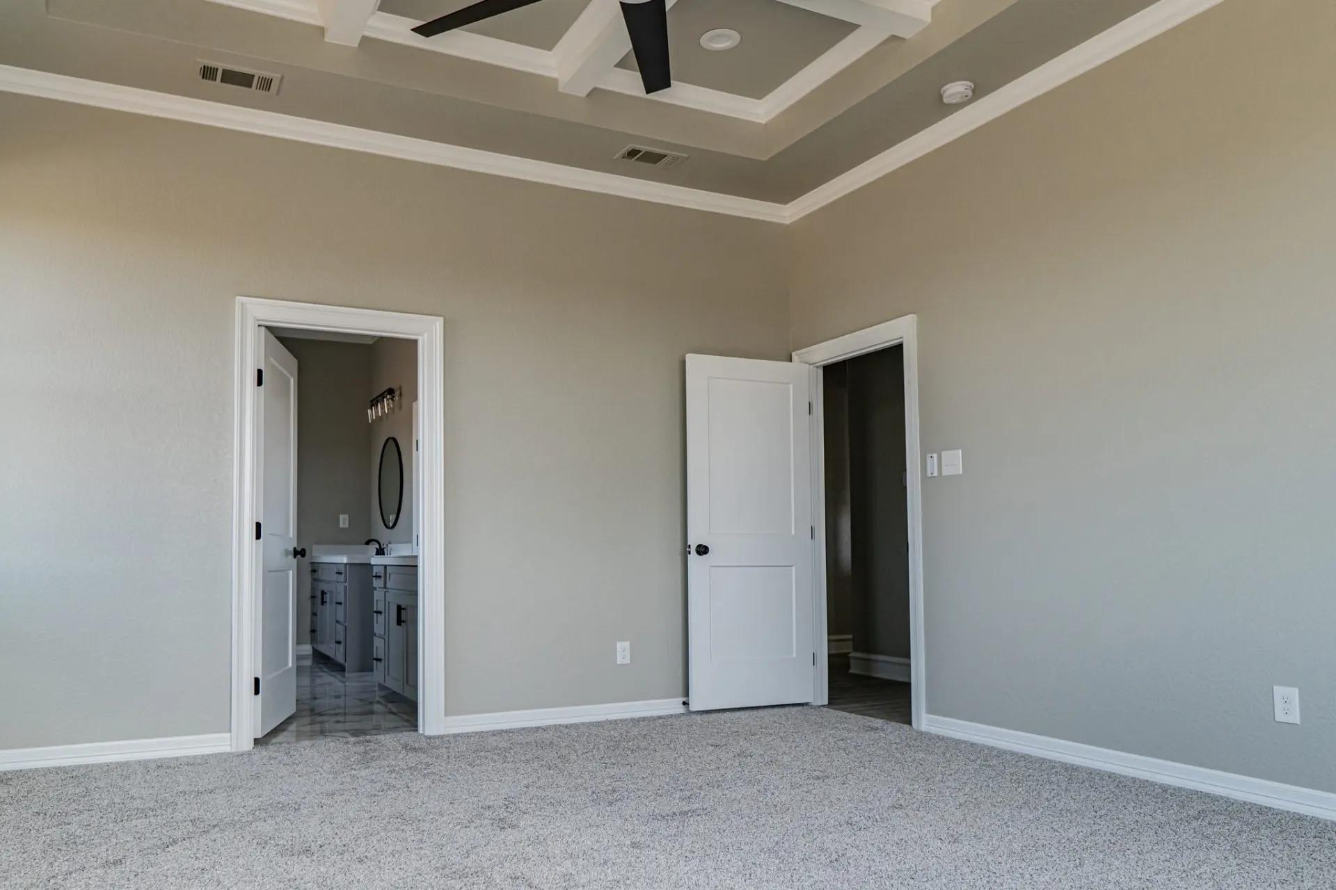 Primary bedroom at the 12th St Home with doors to the ensuite bath and closet beneath the coffered ceiling