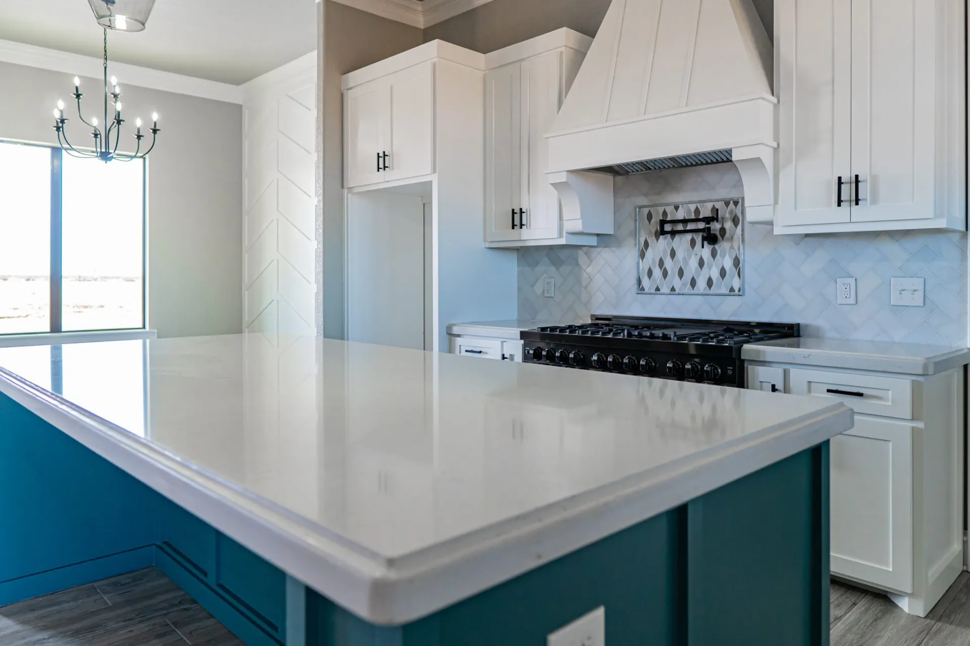 Kitchen at the 12th St Home looking across the teal island to the range wall and chevron accent wall, with a dark iron chandelier over the dining area
