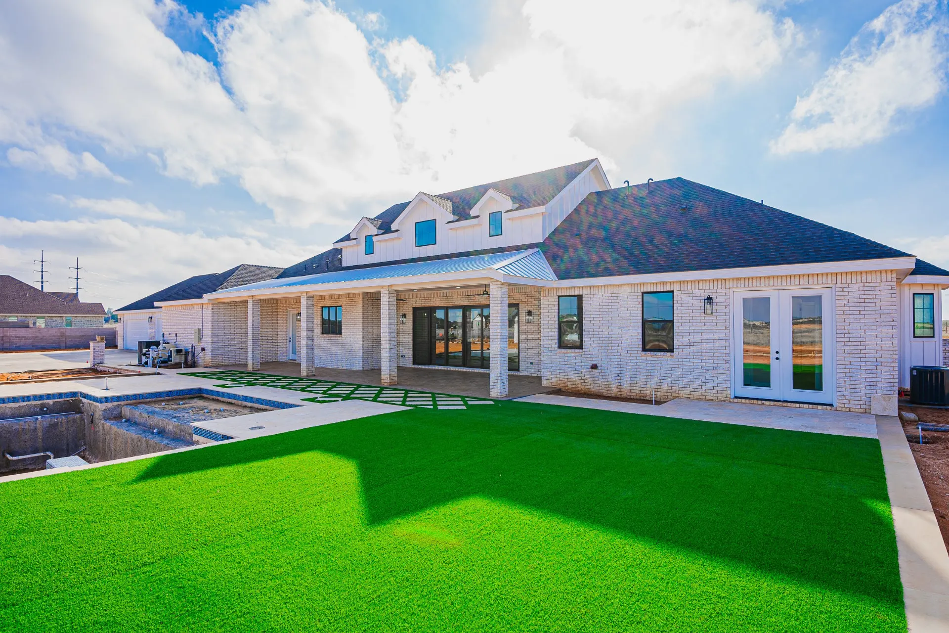 Rear exterior of 1602 NW 12th St with covered patio, artificial turf and pool excavation under way