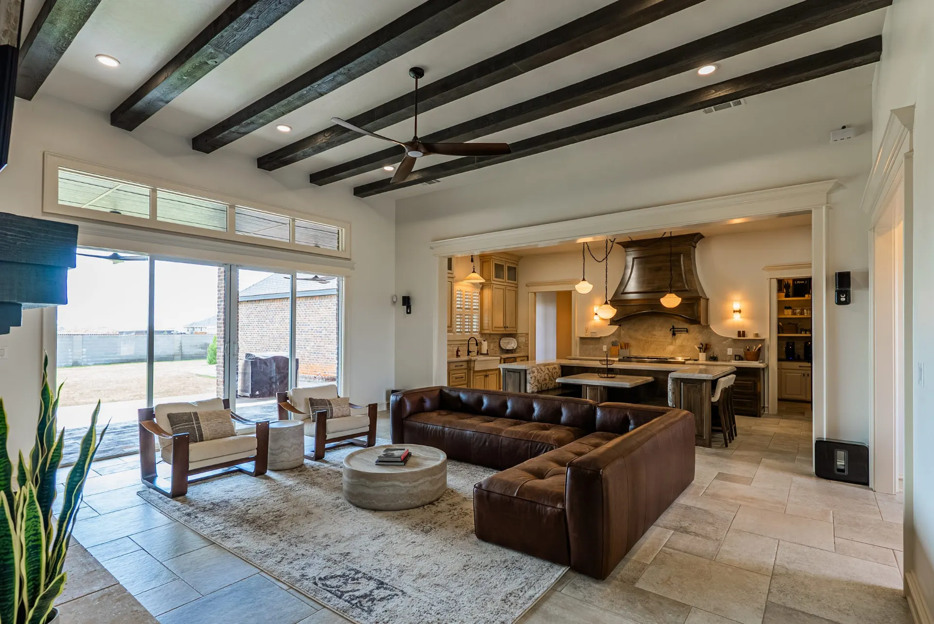 Great room at 1610 NW Eliam Dr opening to the kitchen, with leather sectional and exposed beams