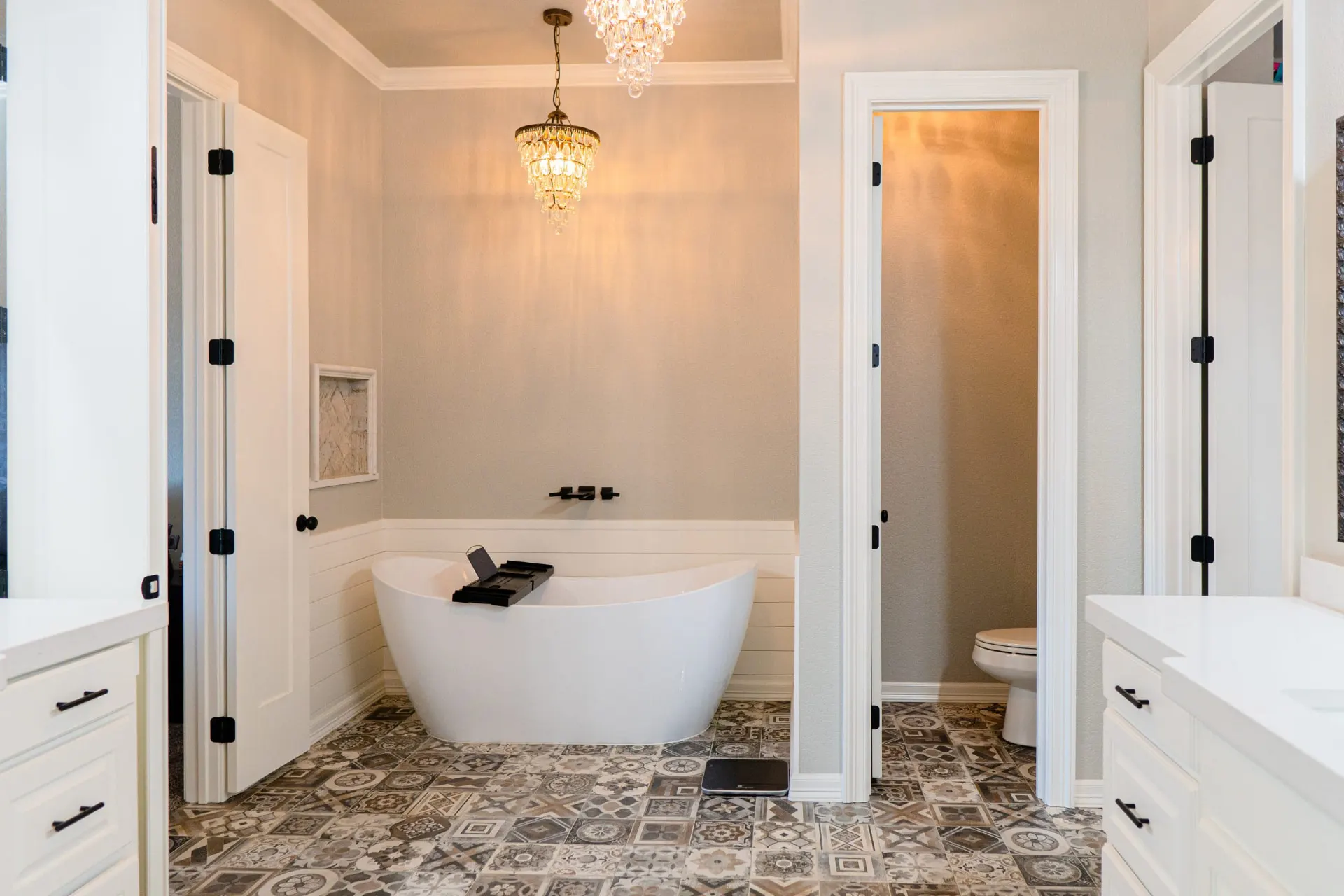 Freestanding tub against white shiplap beneath a crystal chandelier, framed by twin white vanities on patterned tile at 8821 Shawn Dr