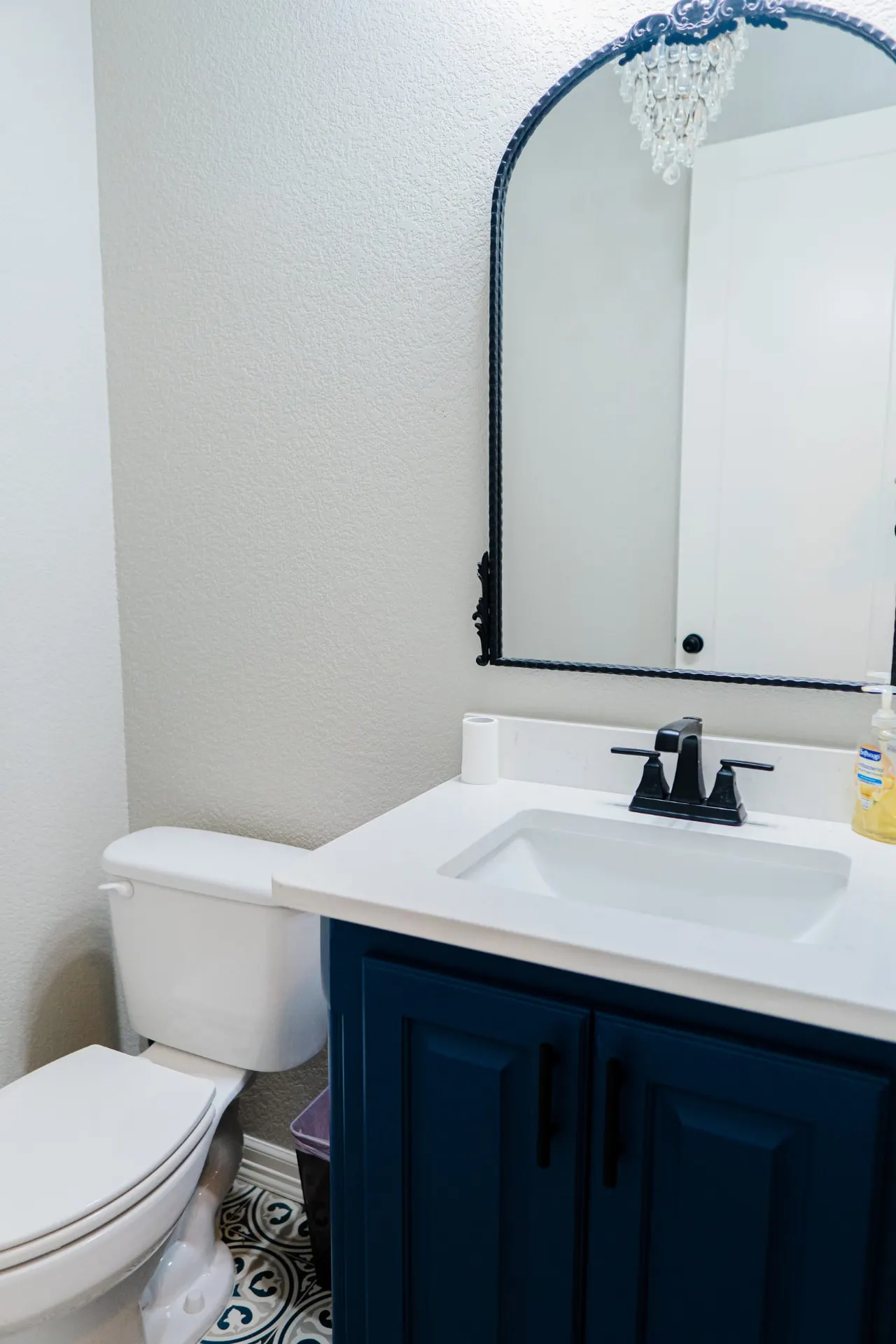 Powder room at 8821 Shawn Dr with a navy vanity, white quartz top, matte black faucet and black arched mirror