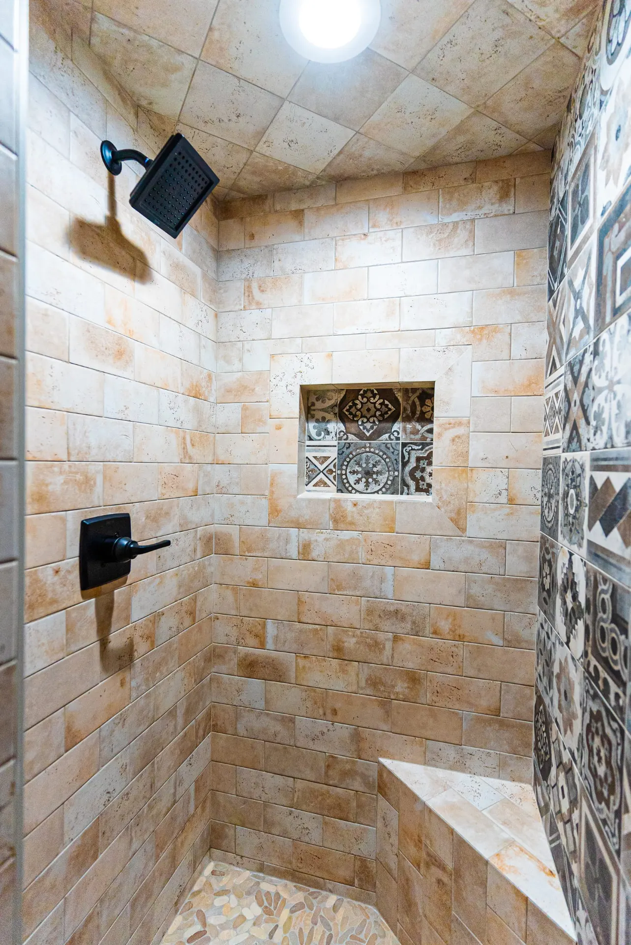 Walk-in shower at 1511 NW 12th St with tan brick tile, decorative niche, pebble floor and matte-black fixtures
