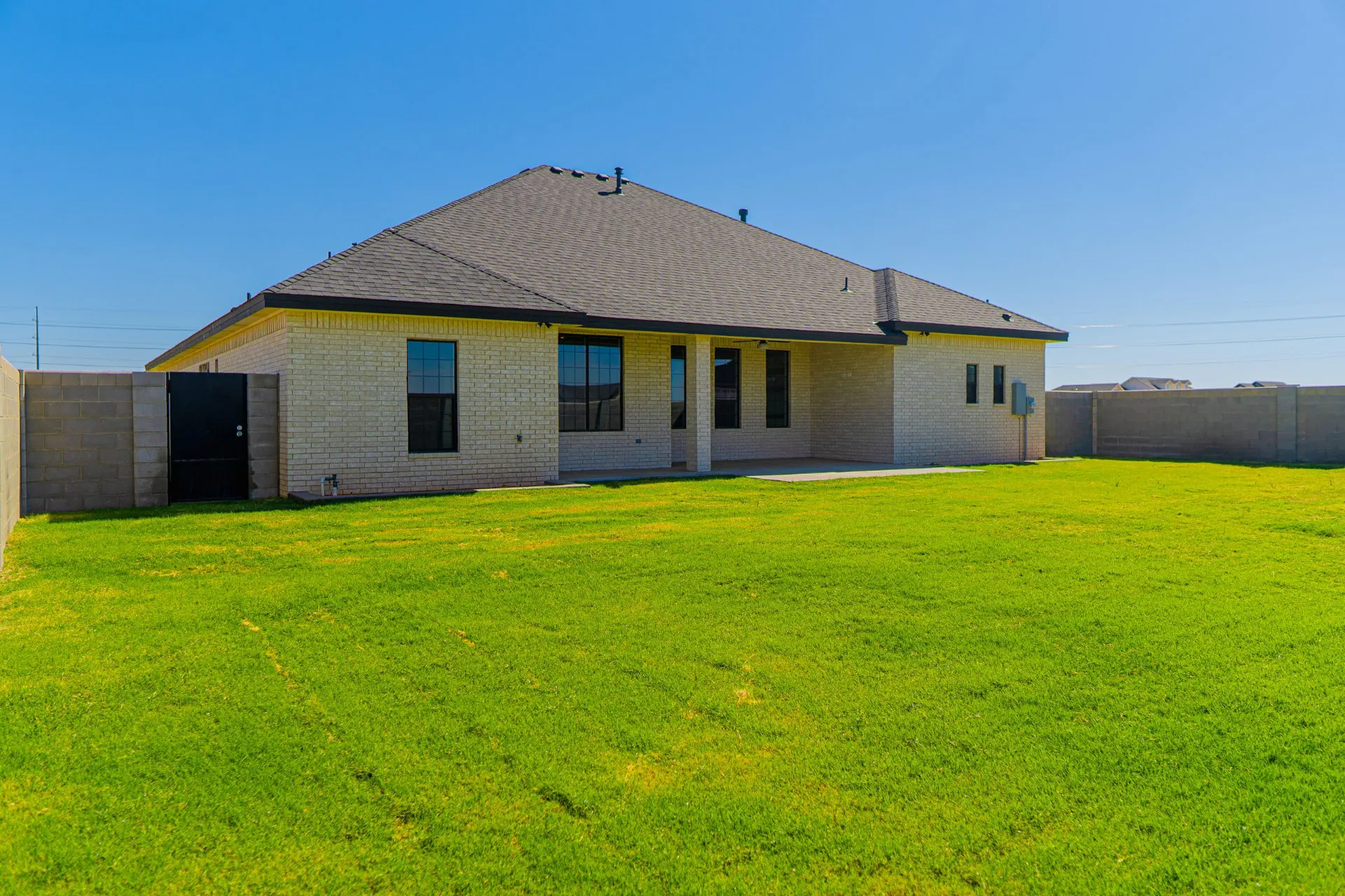 Rear elevation of 1615 NW 12th St with covered patio, black-framed windows and fenced backyard with new sod