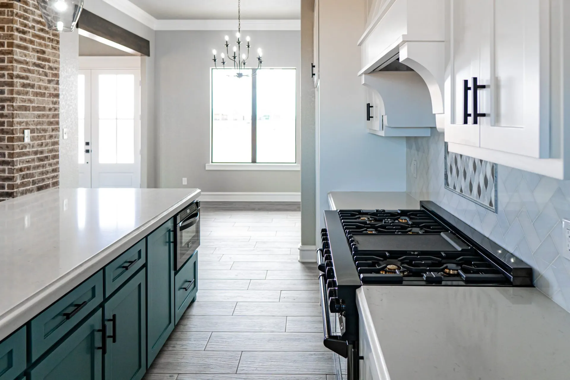 Kitchen at the 12th St Home looking past the teal island and gas range with griddle toward the dining room chandelier and front door