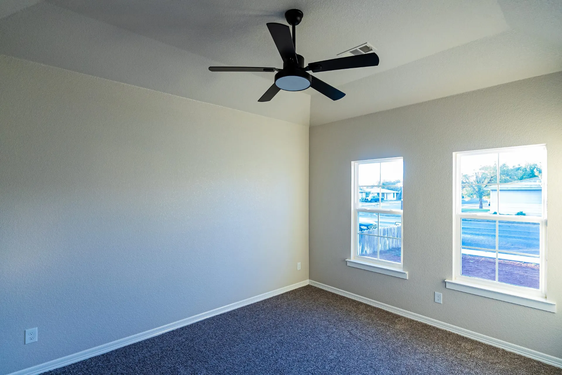 Empty bedroom at 708 K Ave with soft gray walls, white trim, carpet, a black ceiling fan and two windows facing the street