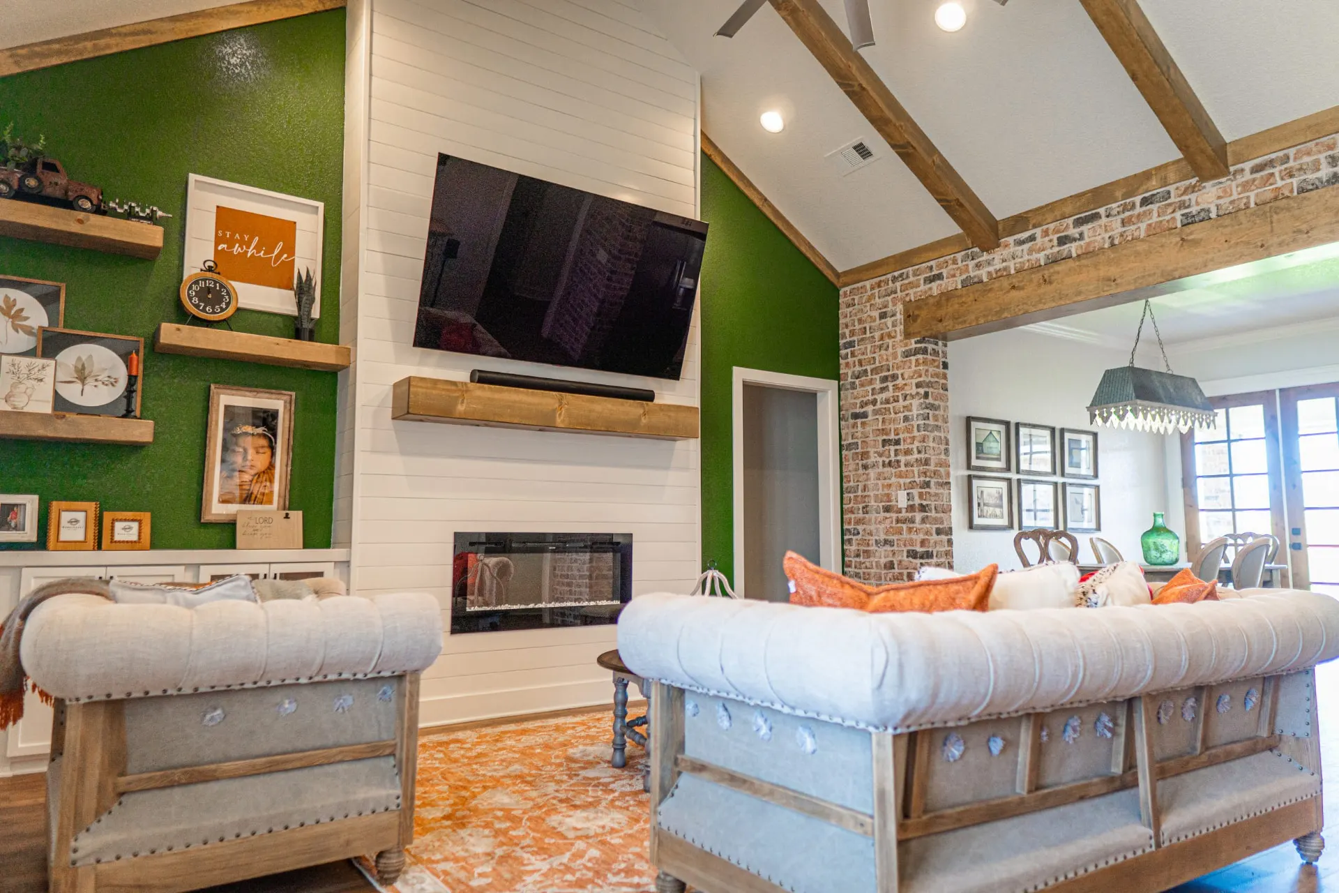 Living room at the K Ave Farmhouse with a deep green accent wall, white shiplap fireplace, mounted TV and cream tufted seating