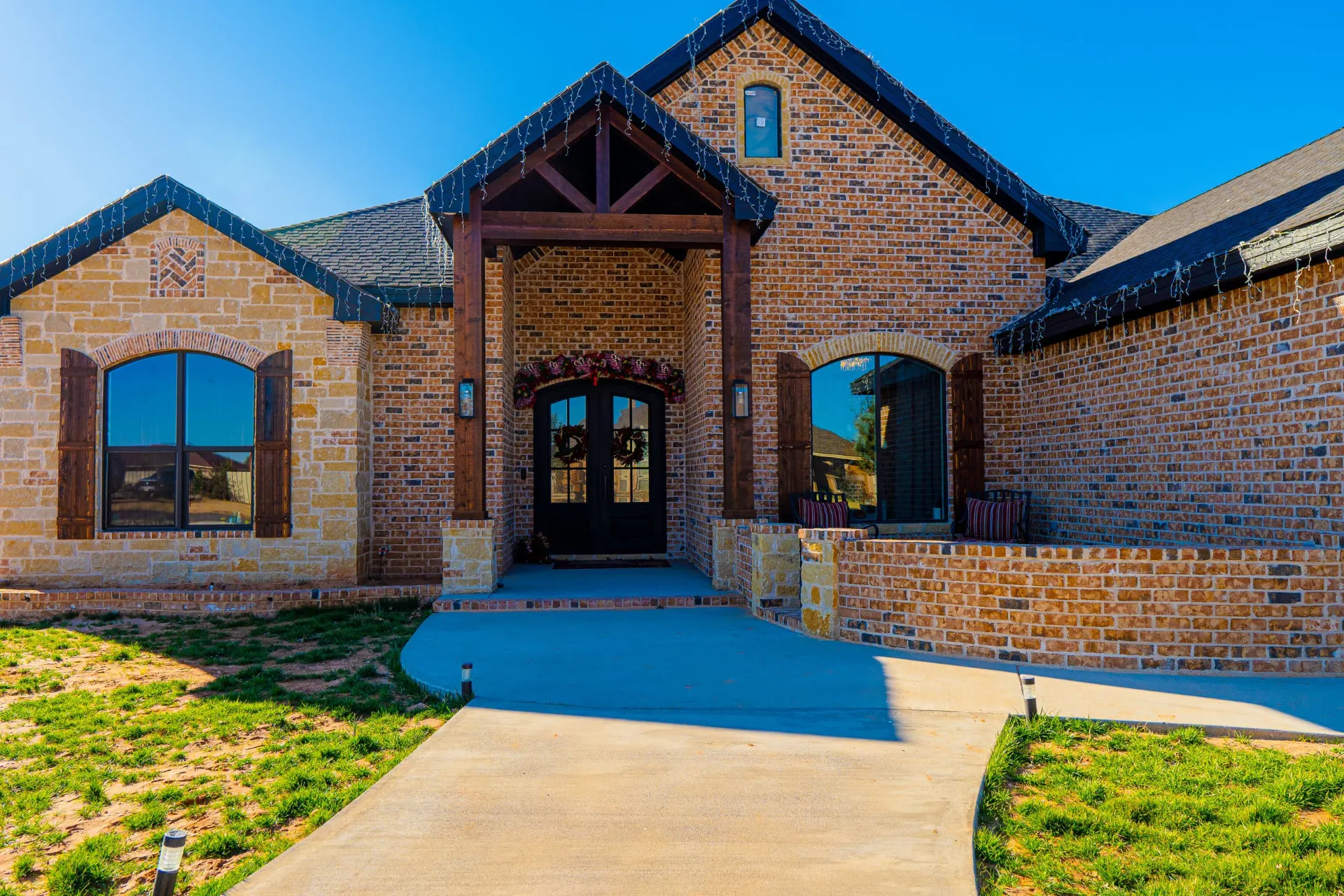 Timber-framed covered entry at 8821 Shawn Dr with arched black double doors between brick and limestone gables