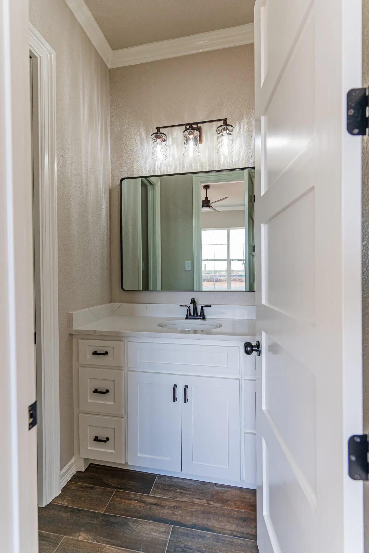 Bathroom vanity at 1602 NW 12th St with white cabinetry, quartz counter, oil-rubbed bronze sconces and wood-look tile floor