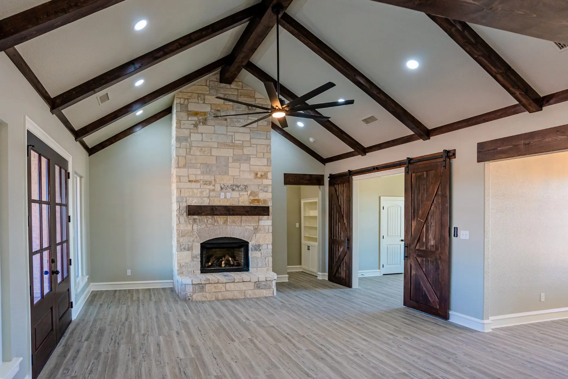 Great room at the Eliam St Home with dark wood trusses over a full-height stone fireplace and barn doors opening to a hallway