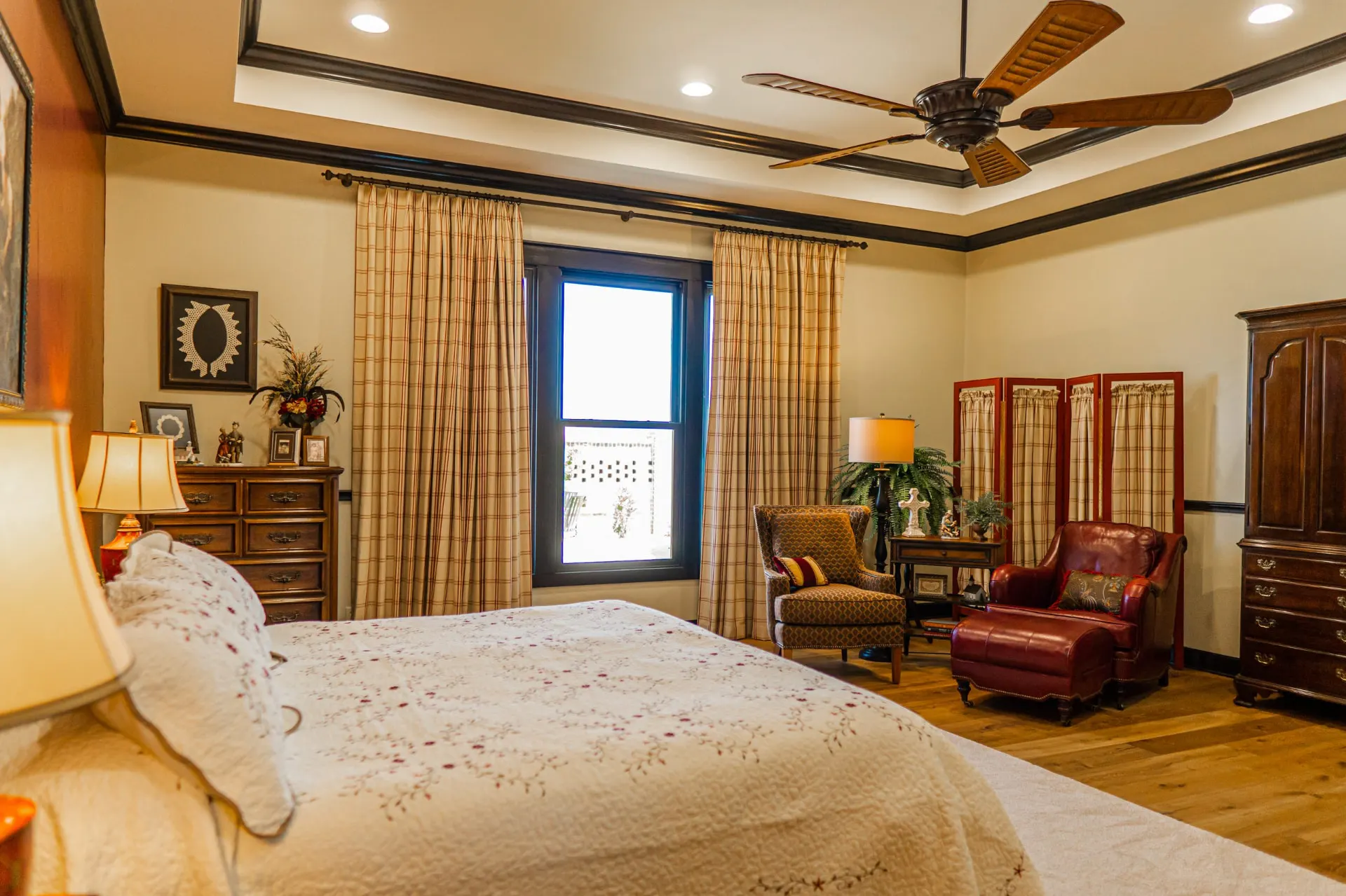 Primary bedroom sitting area at the Wraparound Porch Home with plaid drapery, leather armchair and tray ceiling