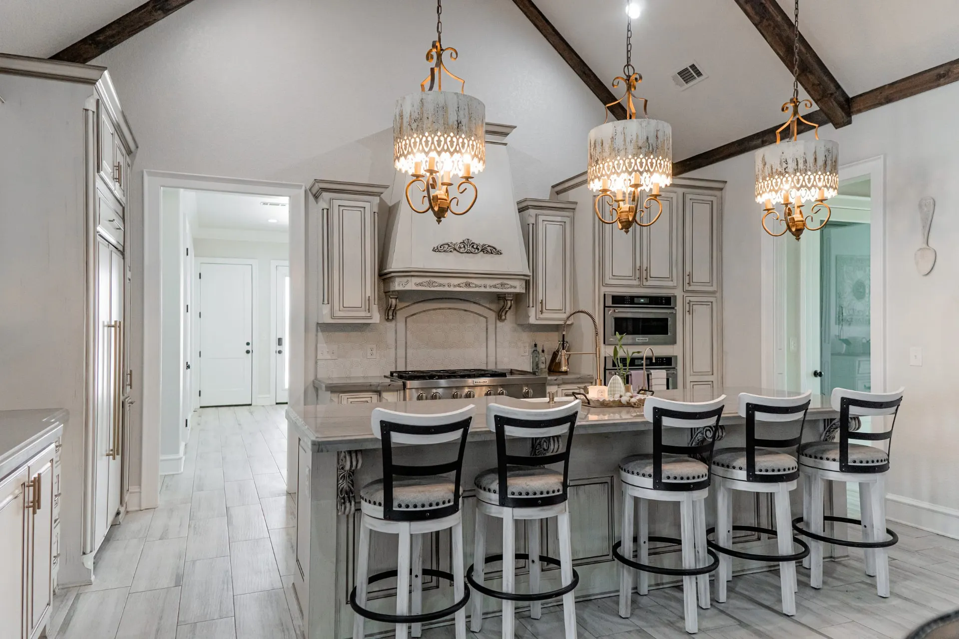 Kitchen at 1667 Eldenrod with antiqued white cabinetry, a carved range hood and three ornate candelabra chandeliers over the island