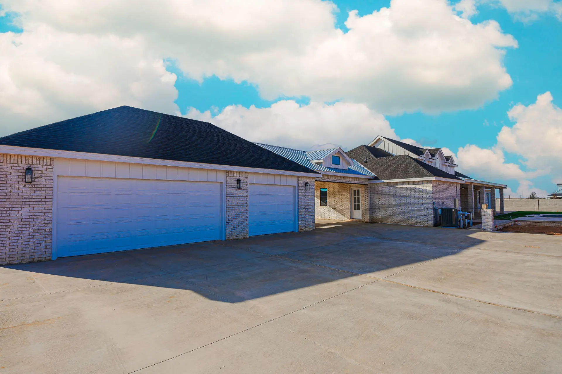 Garage-side elevation of 1602 NW 12th St with light brick, three-car garage and porte-cochère under big sky clouds