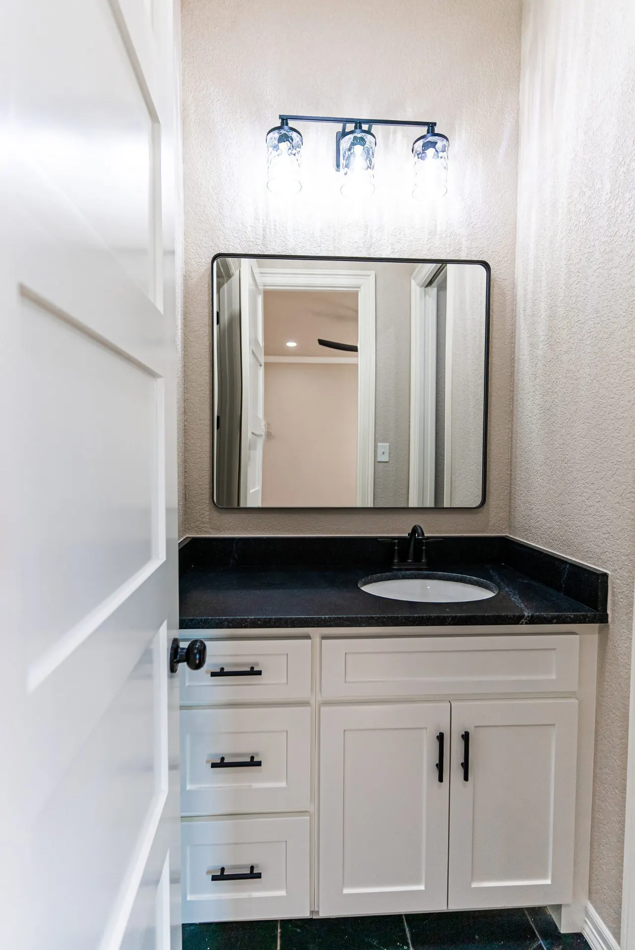 Bathroom vanity at 1602 NW 12th St with white cabinetry, honed black granite counter and glass-shade sconces