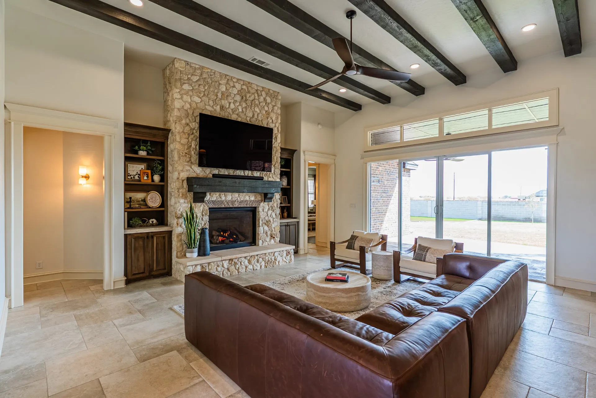 Great room at 1610 NW Eliam Dr with stacked-stone fireplace, dark wood mantel and beamed ceiling