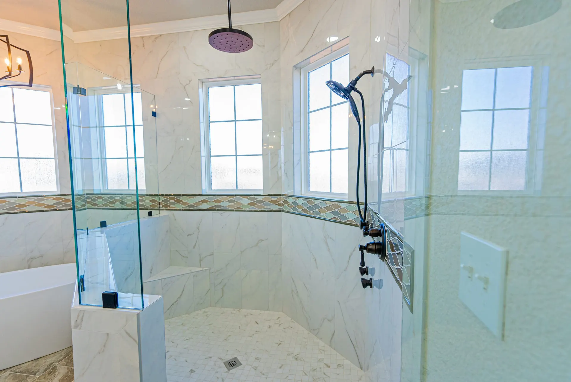 Walk-in shower at 1602 NW 12th St with white marble tile, wave-mosaic accent band and matte-black fixtures