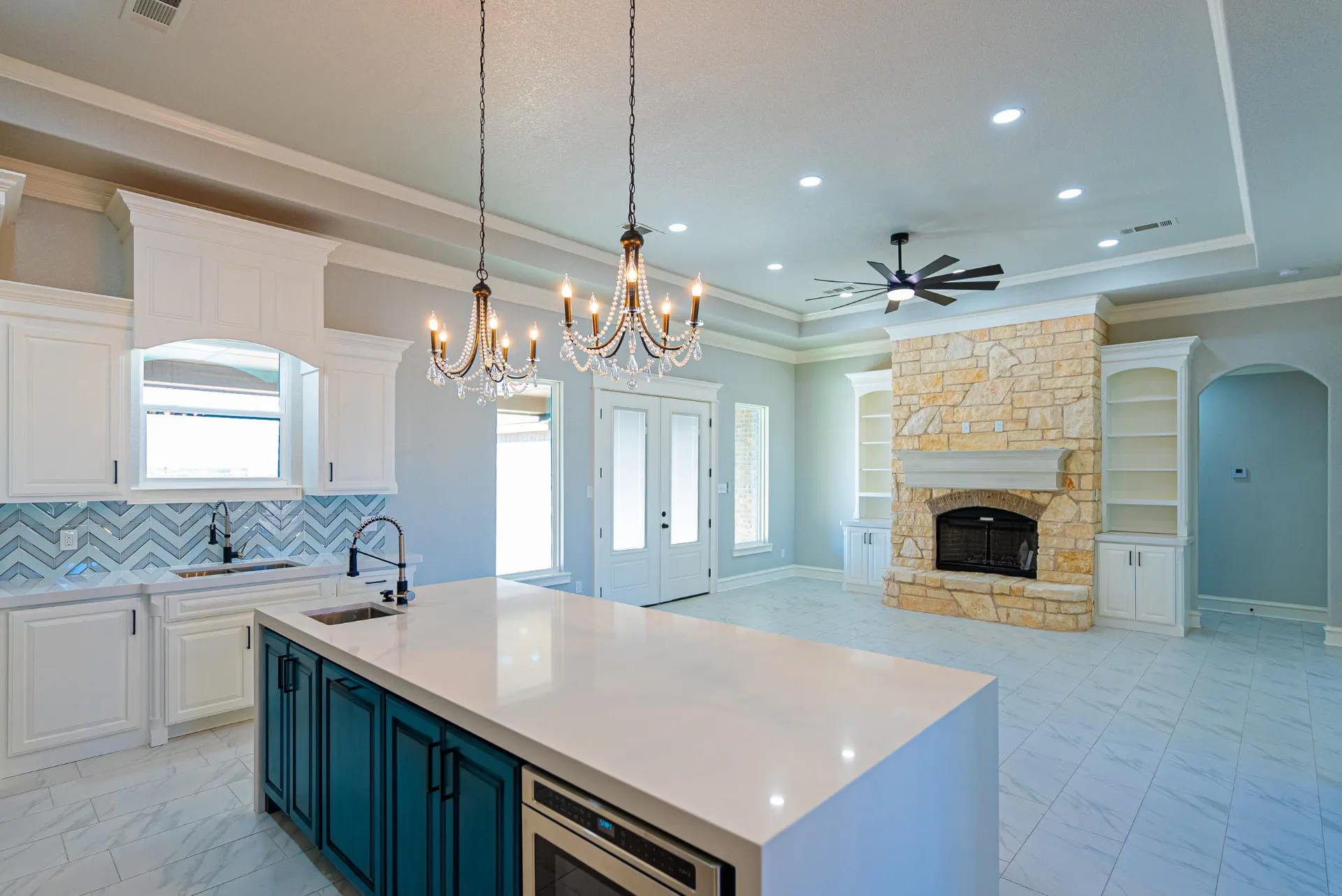 Kitchen and great room at 1511 NW 12th St with chandeliers, French doors and a cream stone fireplace