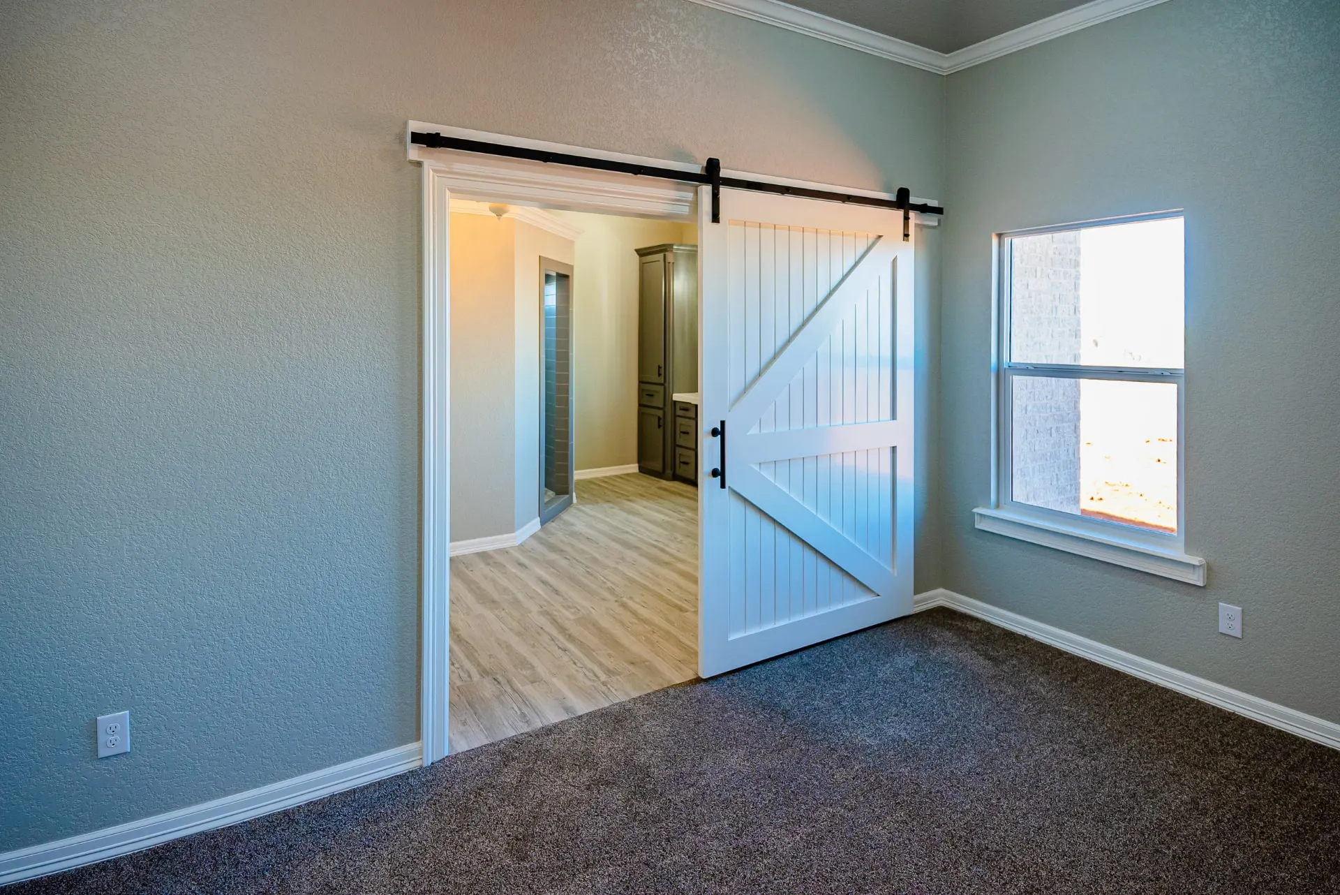 Carpeted bedroom at the Eliam St Home with a white barn door opening to the ensuite bath, beside a window over the backyard