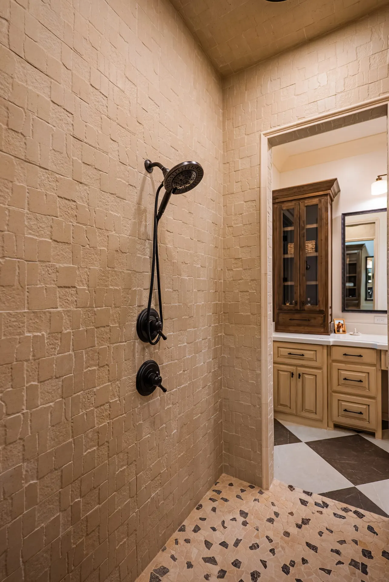 Primary shower at 1610 NW Eliam Dr with chiseled stone tile, bronze fixtures and pebble floor